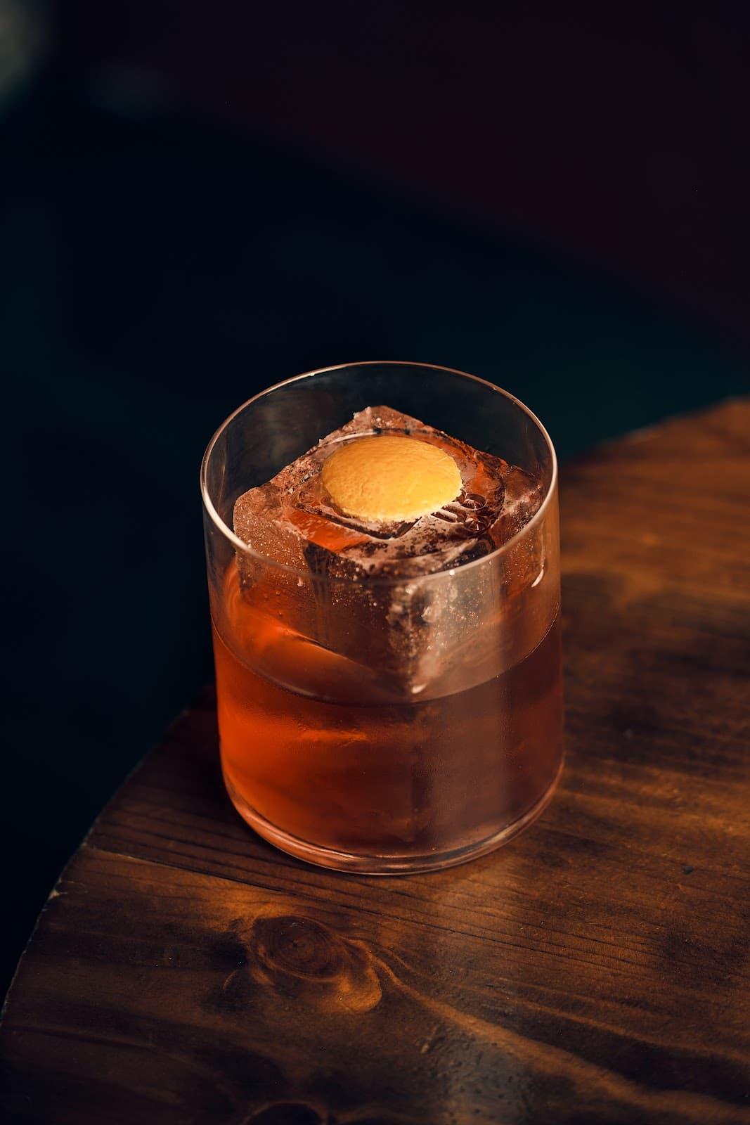 Elegant cocktail with large ice cube and garnish on wooden table in Edinburgh