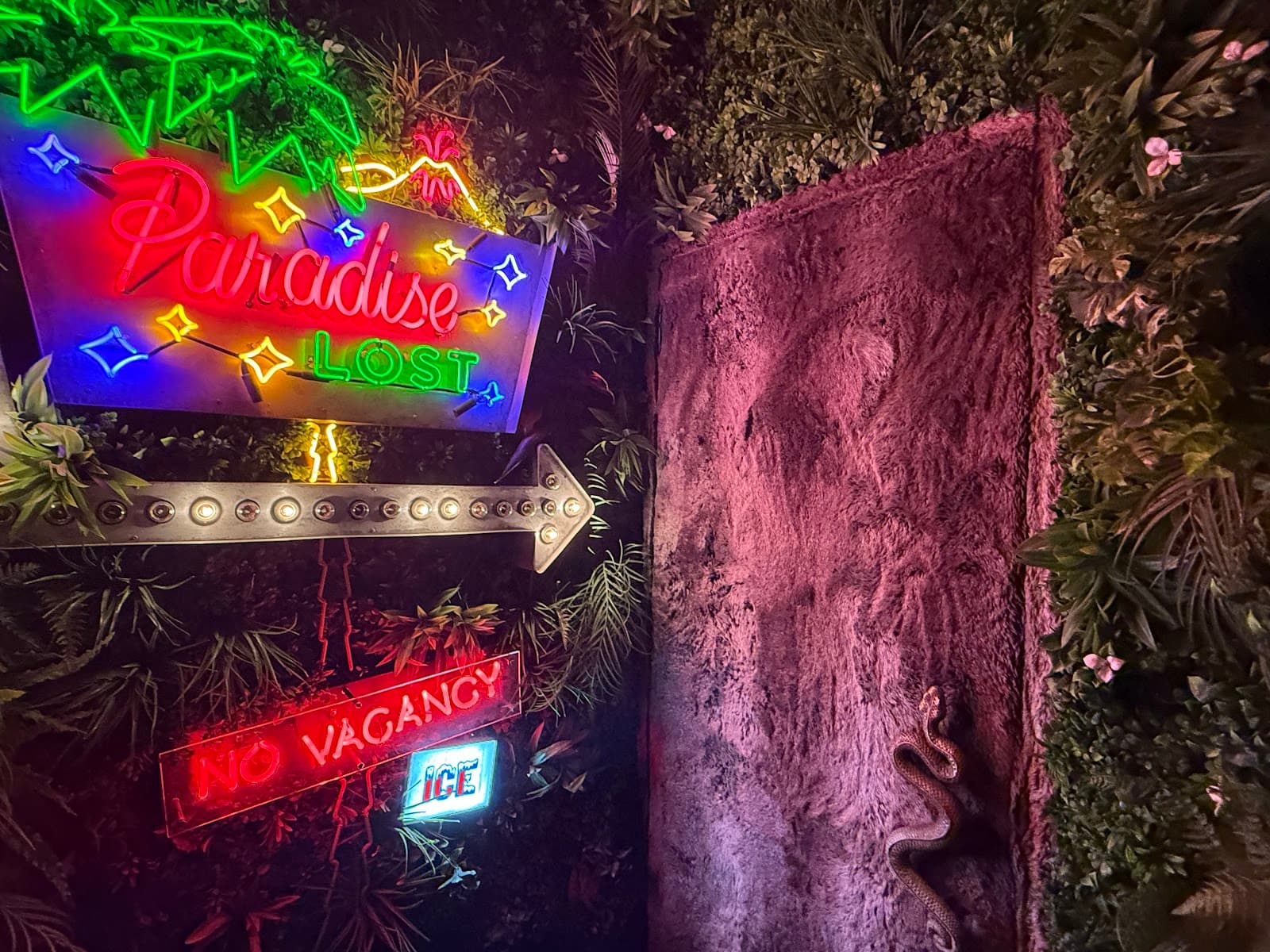 Neon signs reading Paradise Lost and No Vacancy in lush, foliage-filled setting in New York
