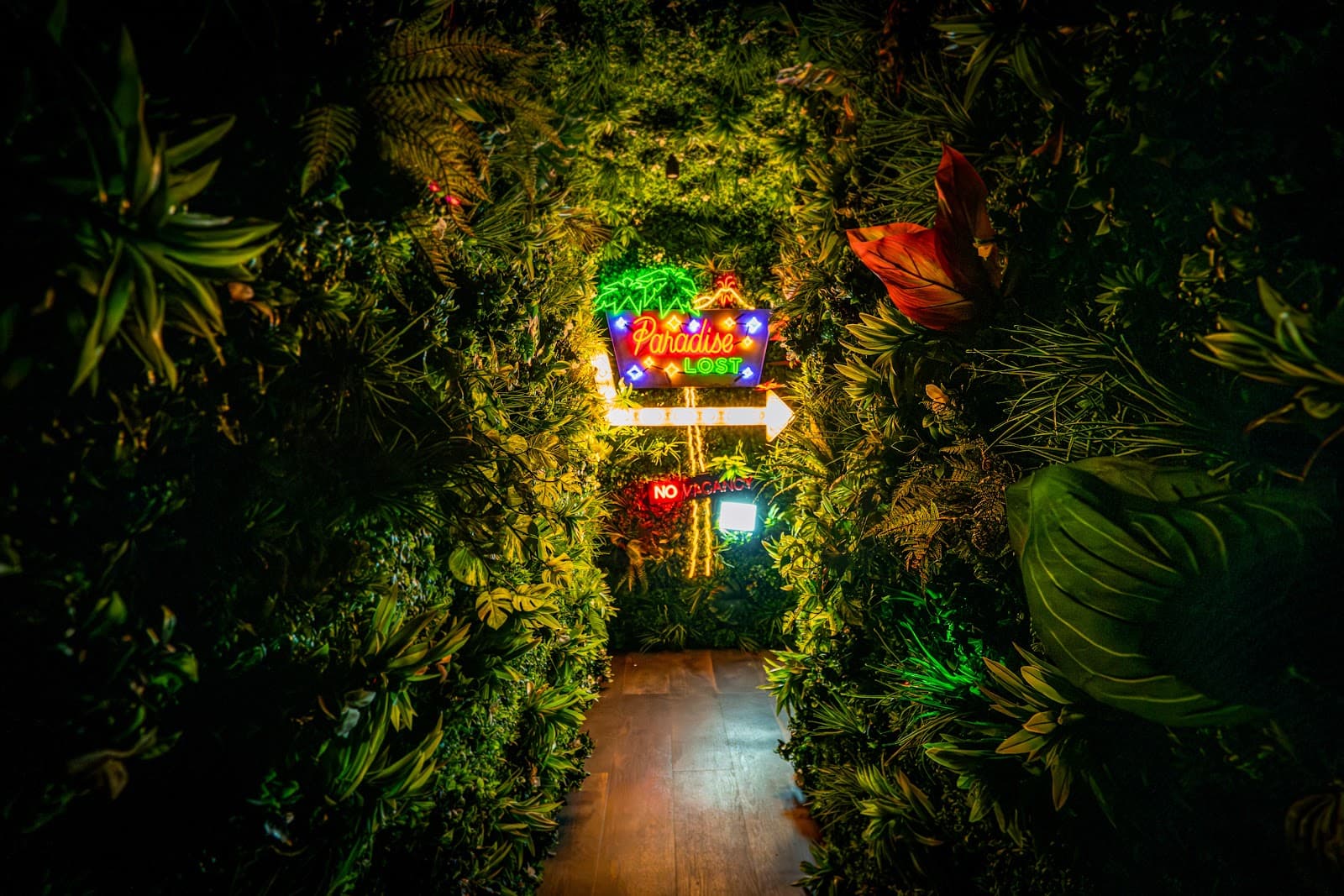 Neon sign in a lush hallway with green plants at Paradise Lost venue in New York