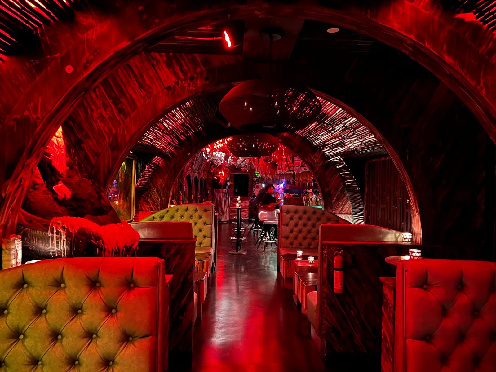 Red-lit interior with arched ceilings and tufted booths in a cocktail bar in New York