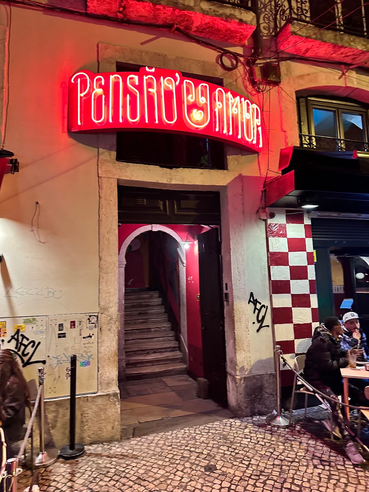 Entrance of Pensao Amor with neon sign and outdoor seating in Lisboa