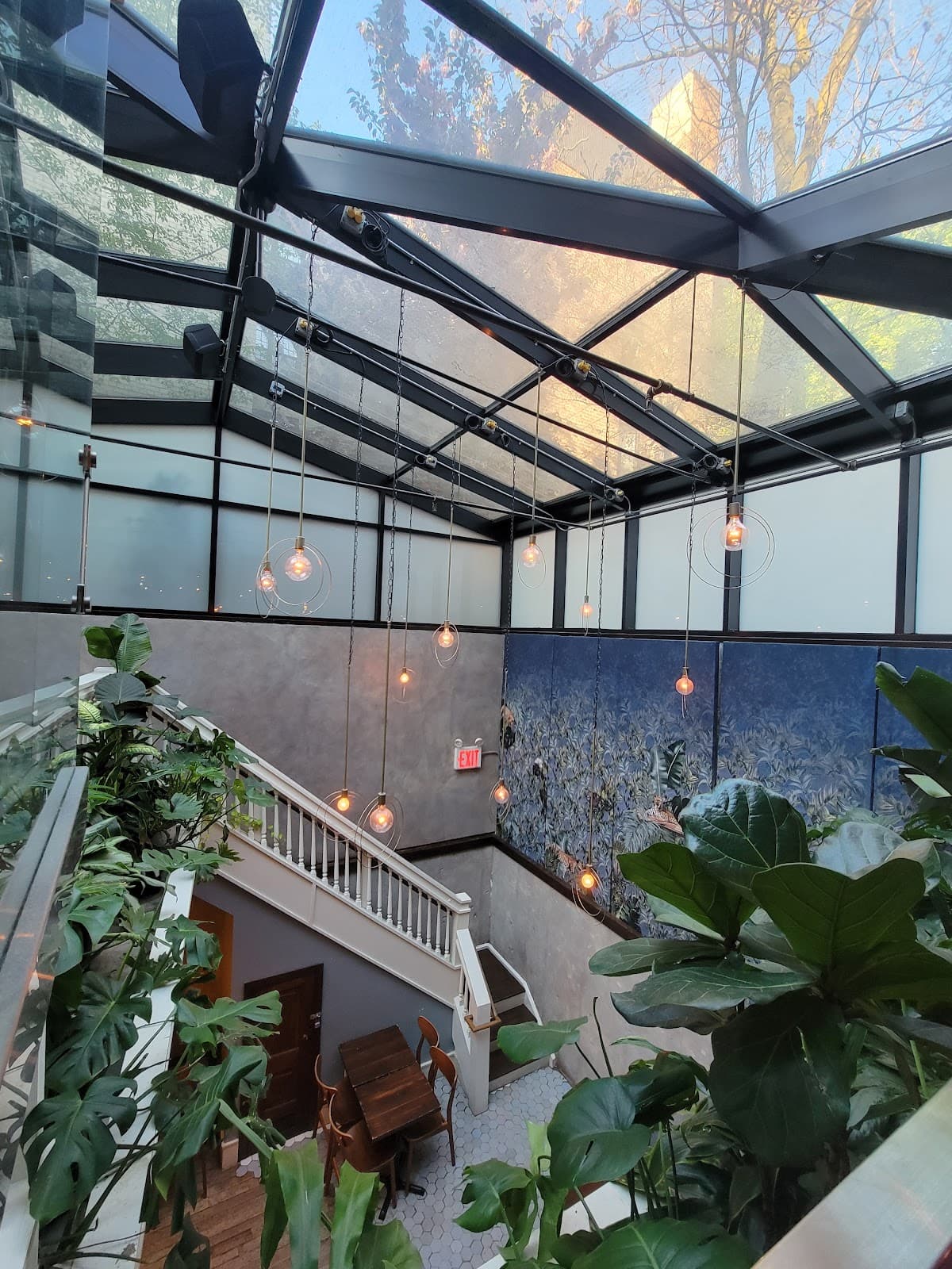Chic interior with skylight, hanging lights, plants, and stairs in a cocktail bar in New York