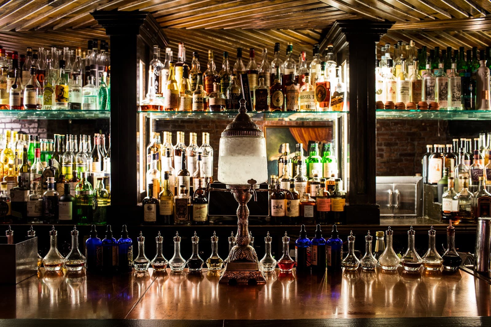 Well-stocked bar counter with an ornate absinthe fountain in dim lighting