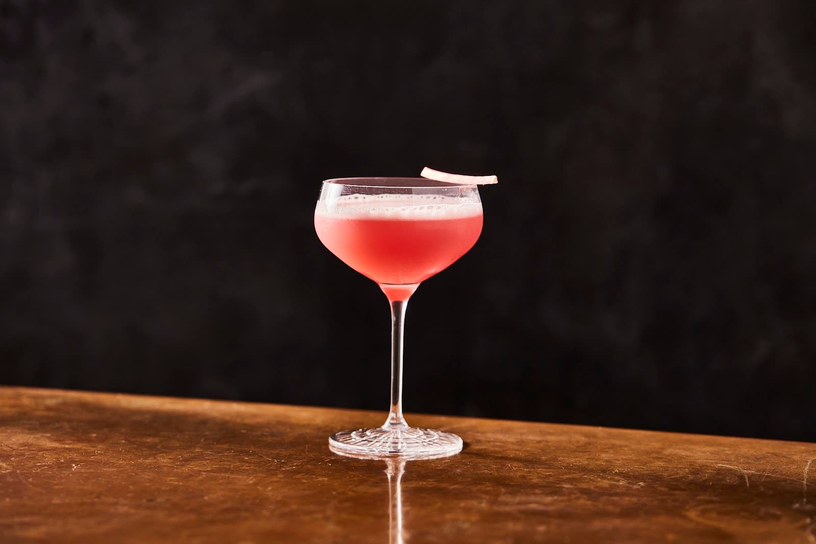 Elegant cocktail glass with pink drink on wooden bar counter in New York