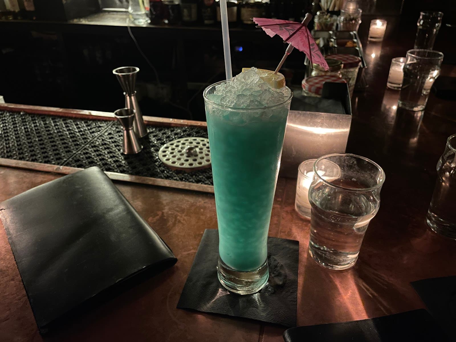 Blue cocktail with umbrella on dimly lit bar counter in New York
