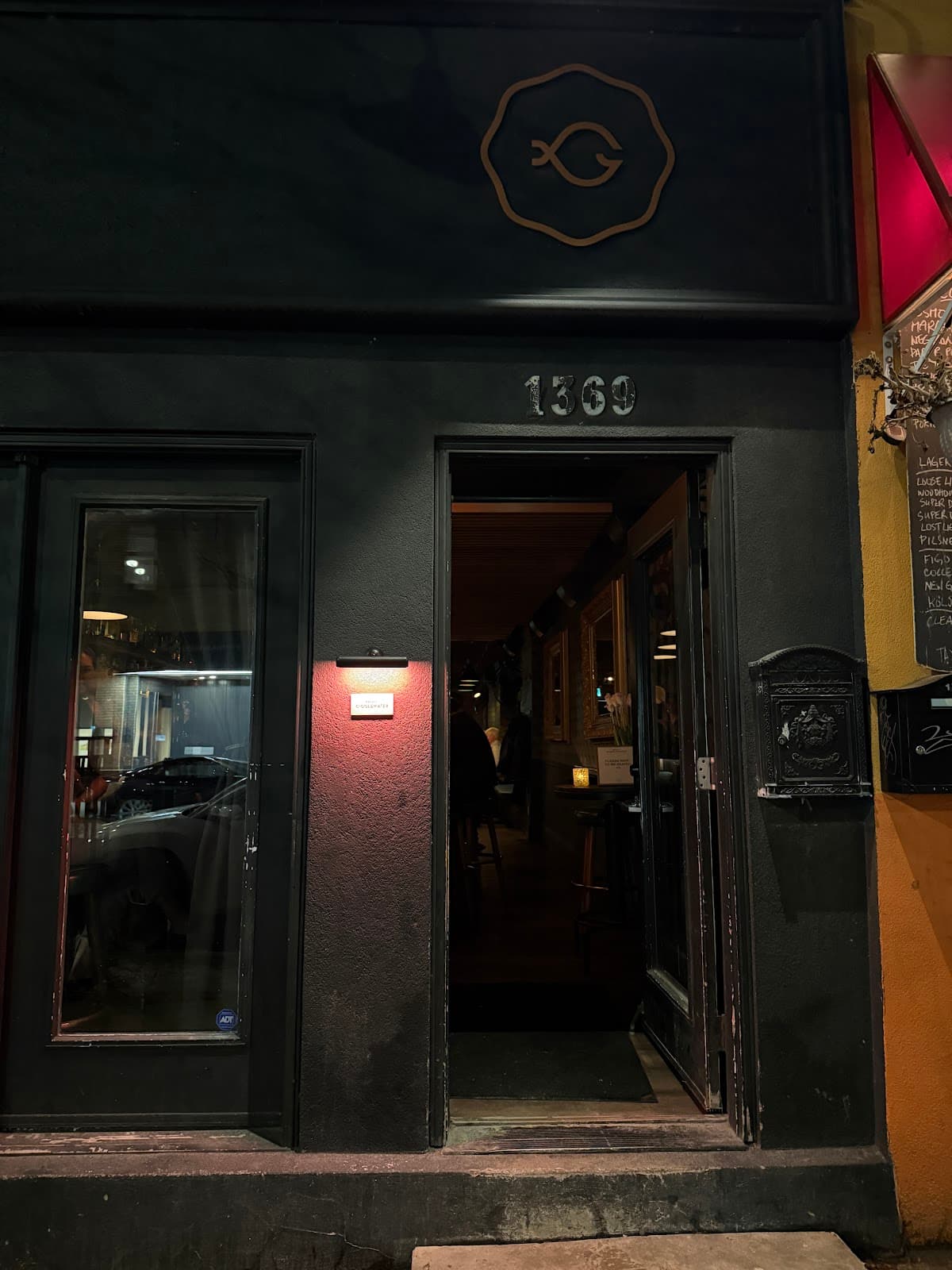 Entrance of a cocktail bar with dim lighting and visible logo above door in Toronto