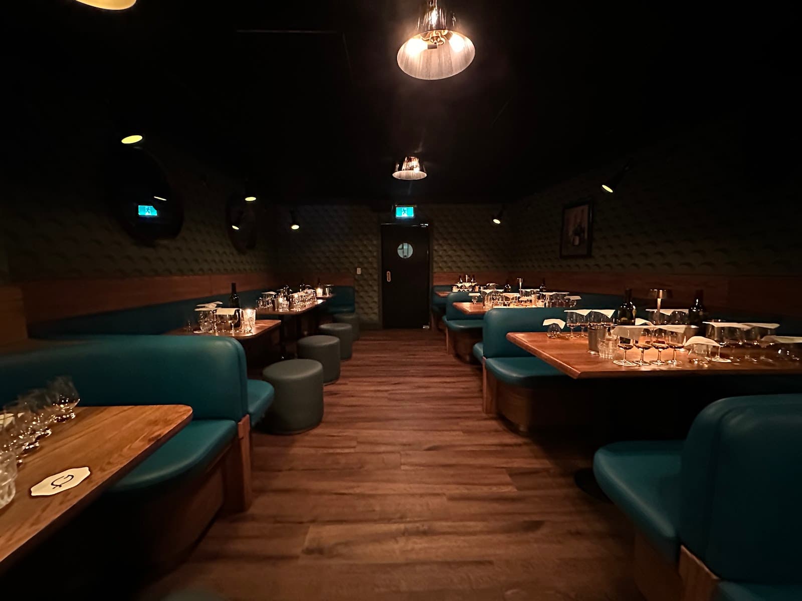 Cozy bar interior with teal booths and wooden tables under dim lighting in Toronto