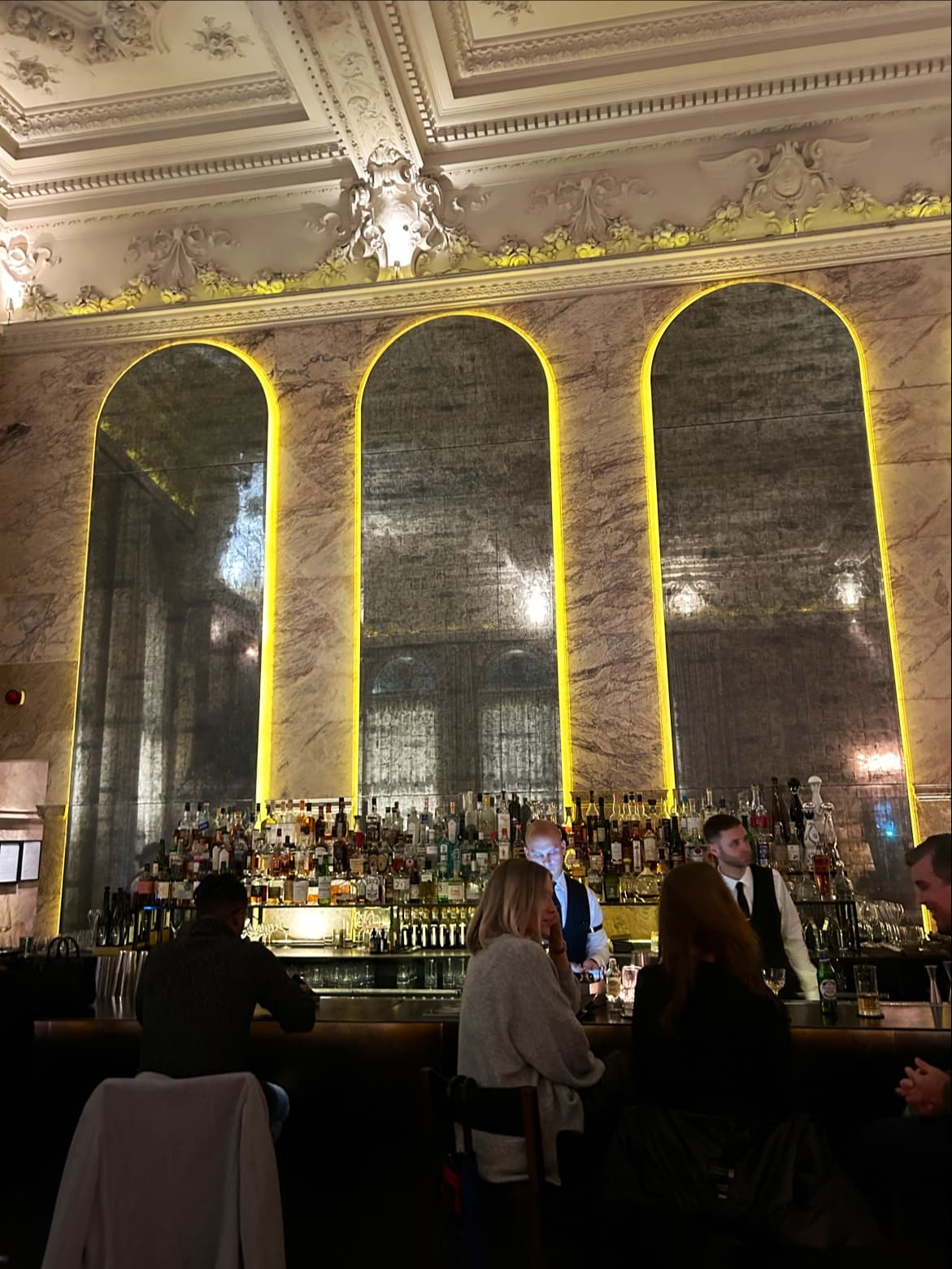 Elegant bar interior with ornate ceiling and patrons seated at the counter in London
