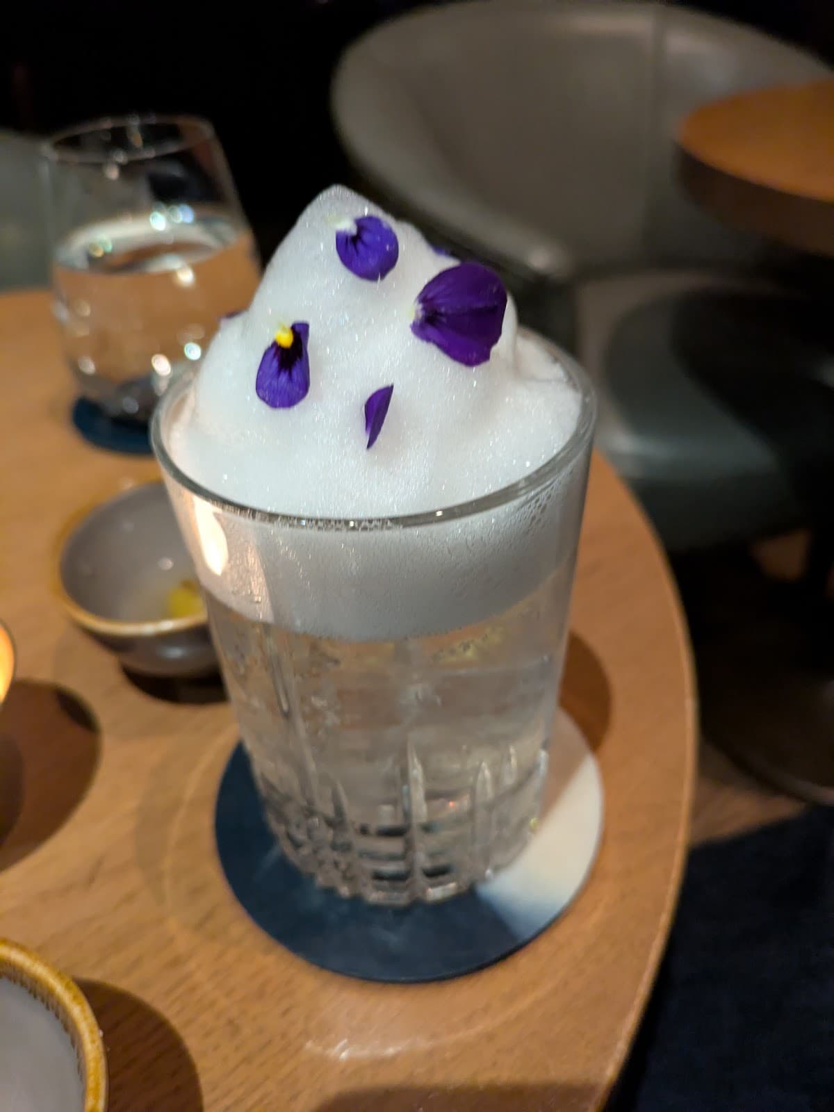 Cocktail with foam and purple flower petals on a wooden table in London