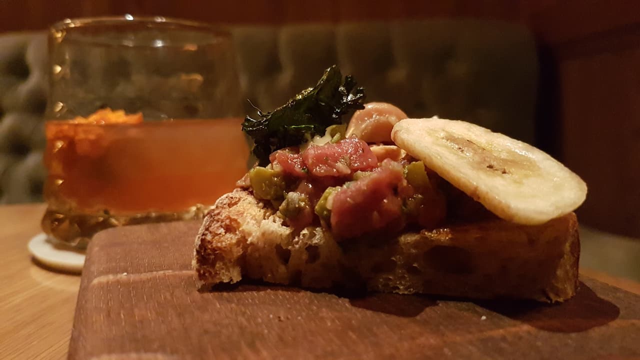 Close-up of a cocktail with a garnished toast on a wooden board in London