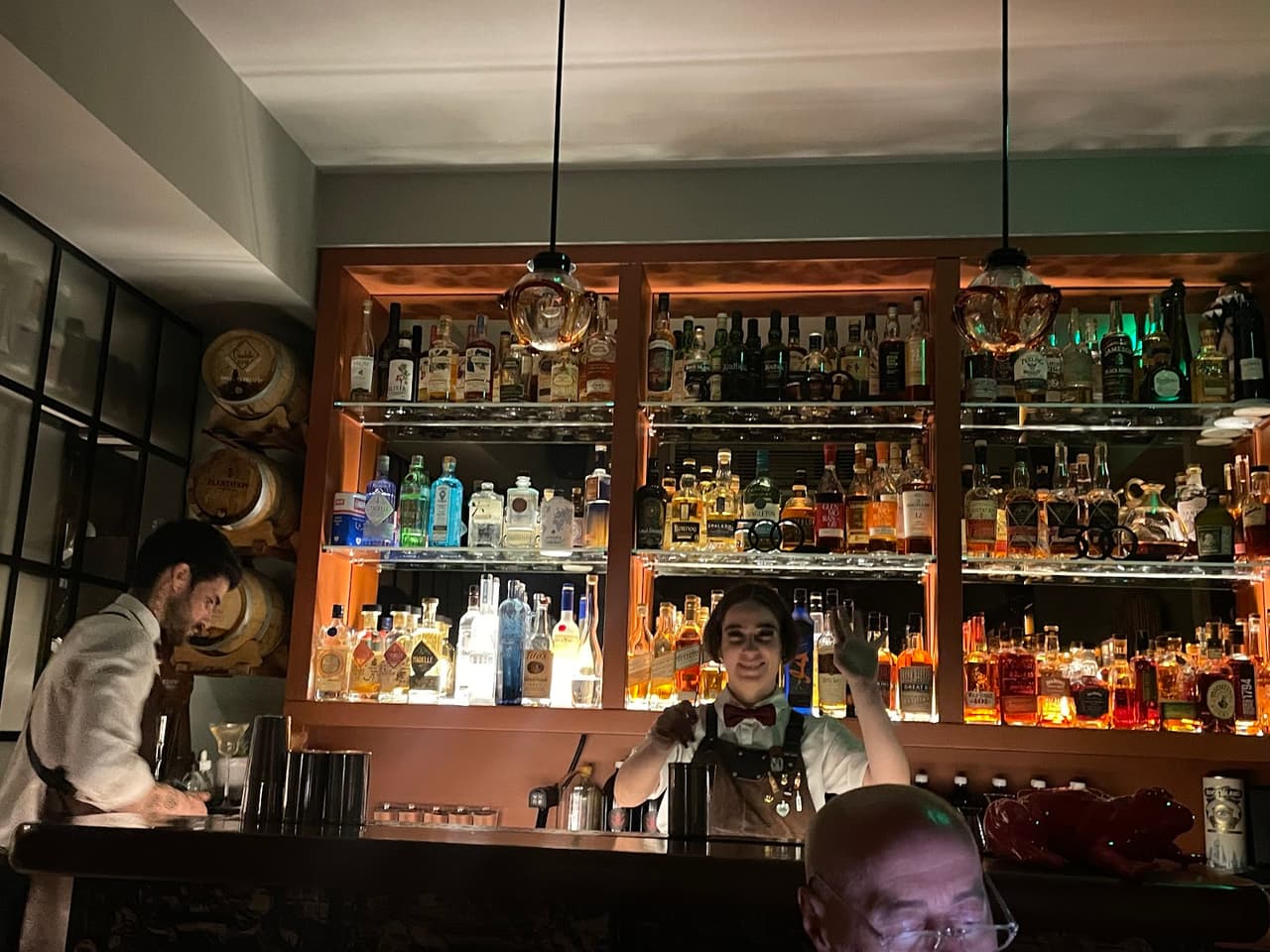 Bartenders preparing drinks at a well-stocked bar with bottles and barrels visible in Lisboa