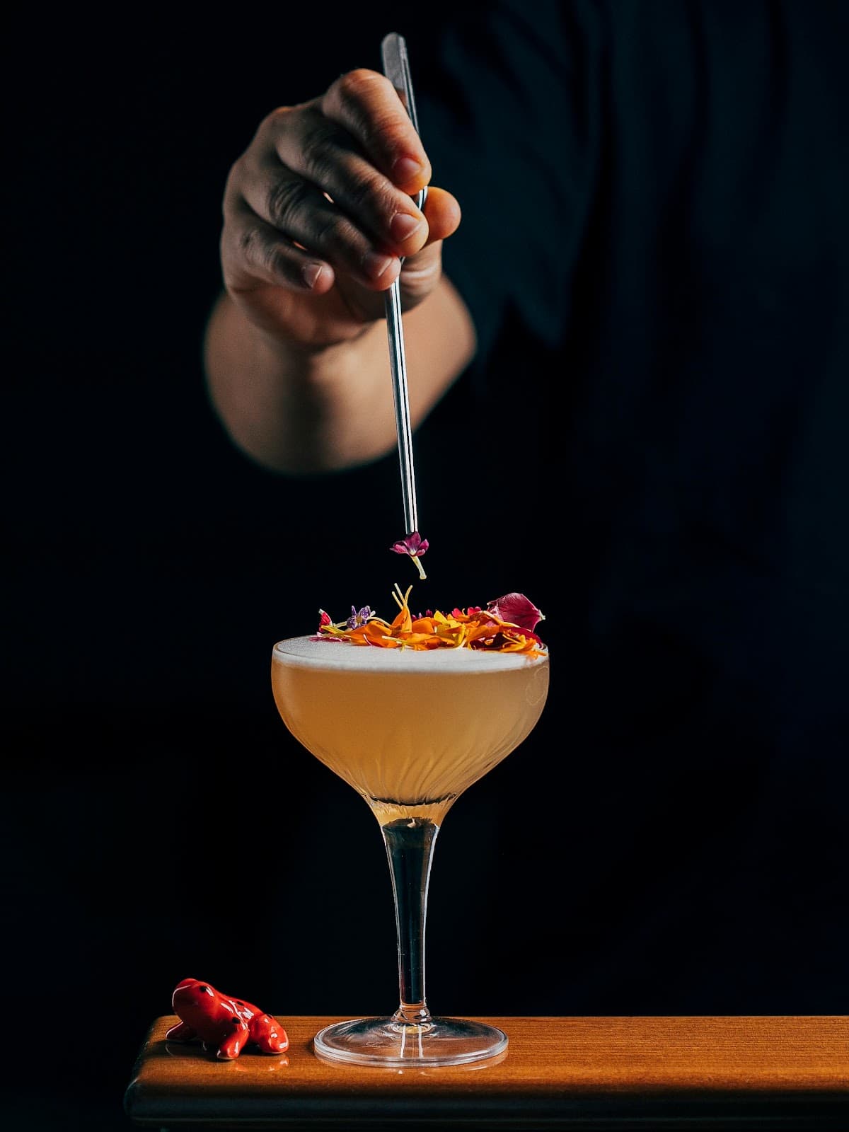 Garnished cocktail in a coupe glass with hand placing flower on top in Lisboa