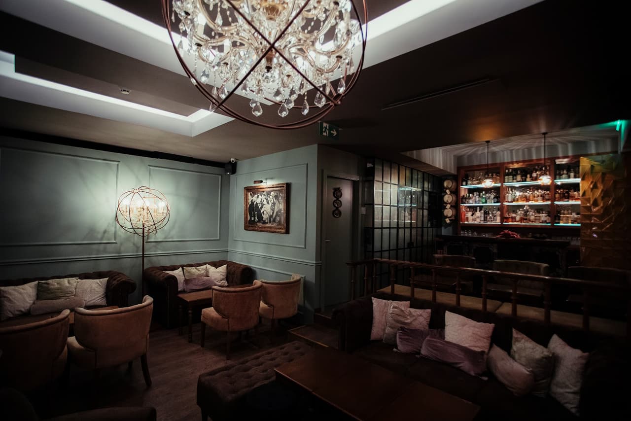 Chic cocktail bar interior with chandeliers, plush seating, and a well-stocked bar