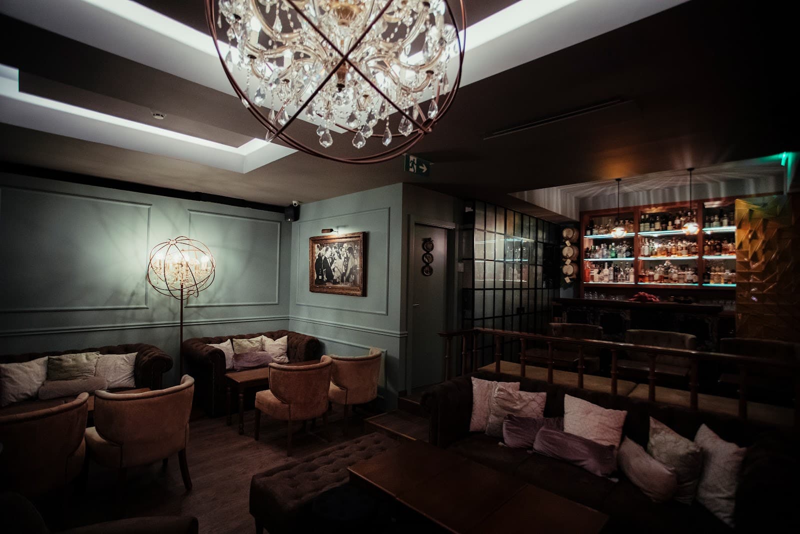 Chic cocktail bar interior with chandeliers, plush seating, and a well-stocked bar