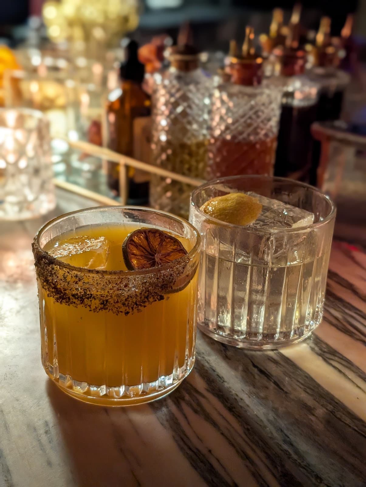 Two cocktails on marble bar with blurred bottles in background in New York
