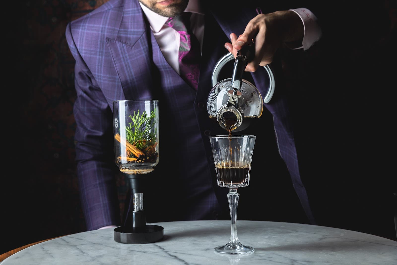 Bartender in a suit pouring cocktail into a glass at a marble table in New York