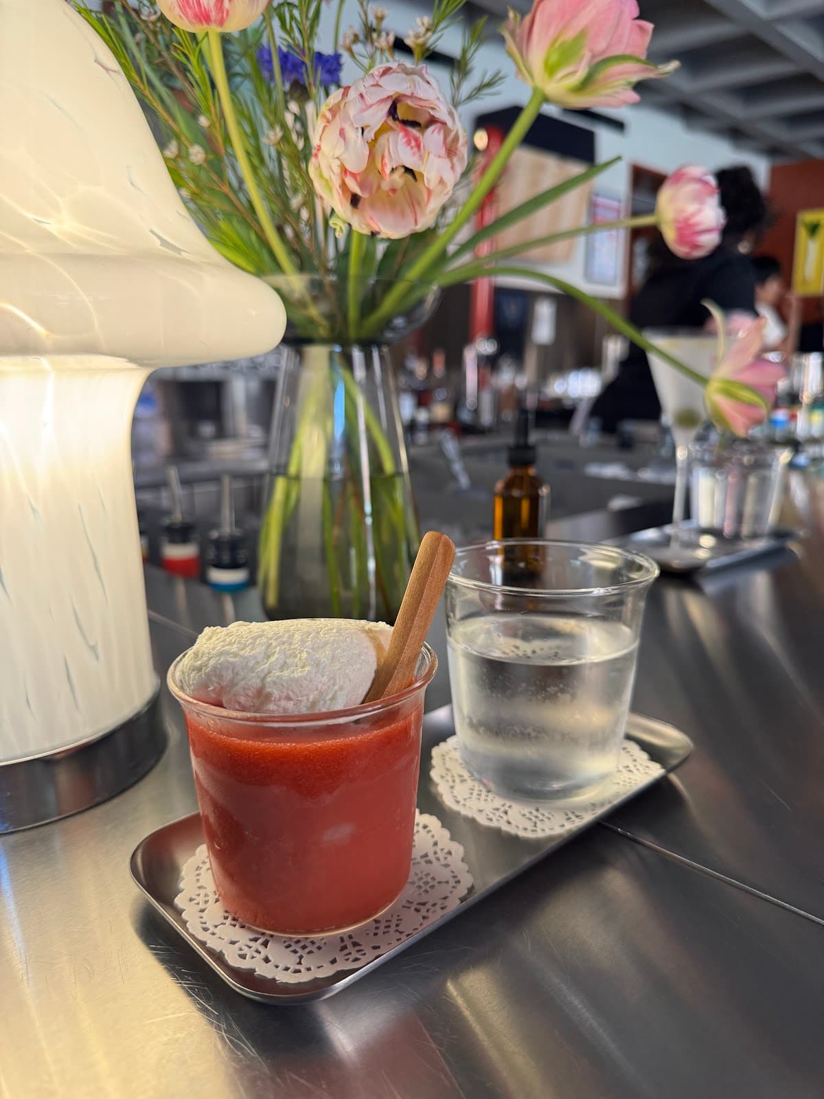 Cocktail with whipped topping on a bar tray with glass and flowers in background in New York