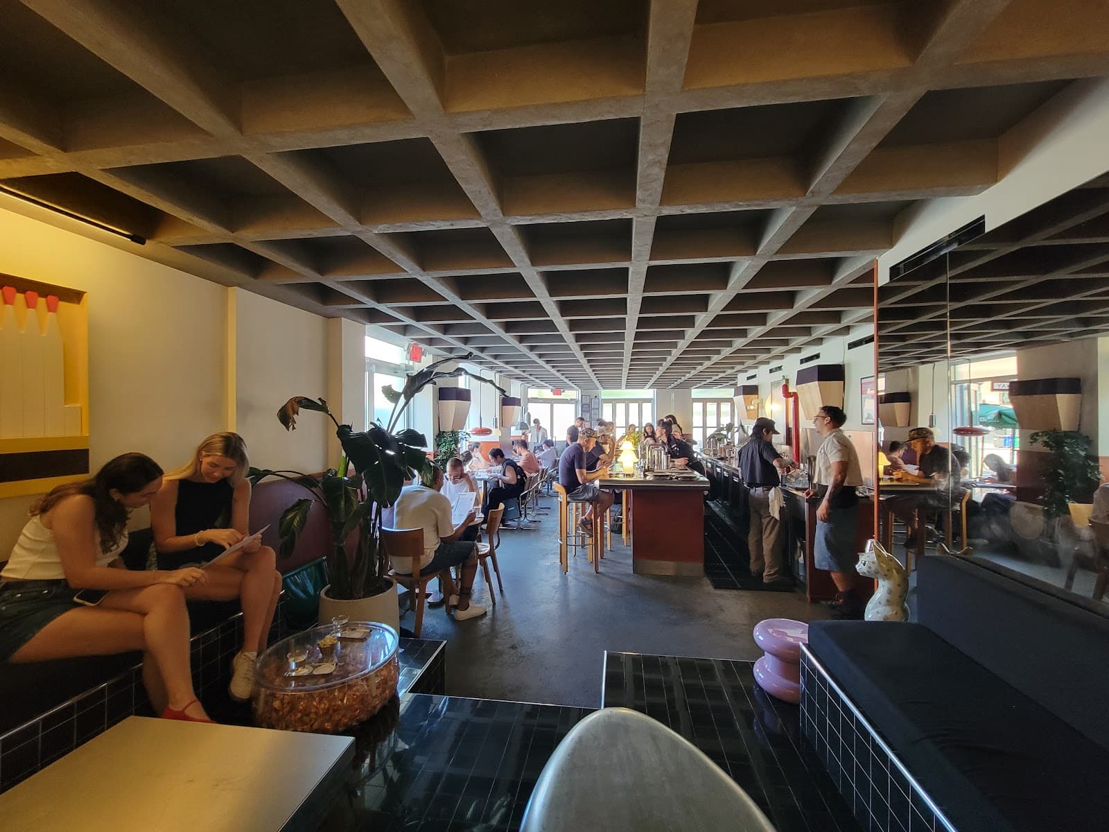 Modern bar interior with patrons seated and bartenders serving drinks