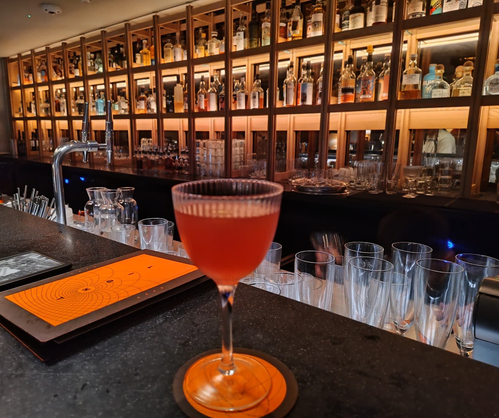Cocktail on bar counter with shelves of bottles in background in London