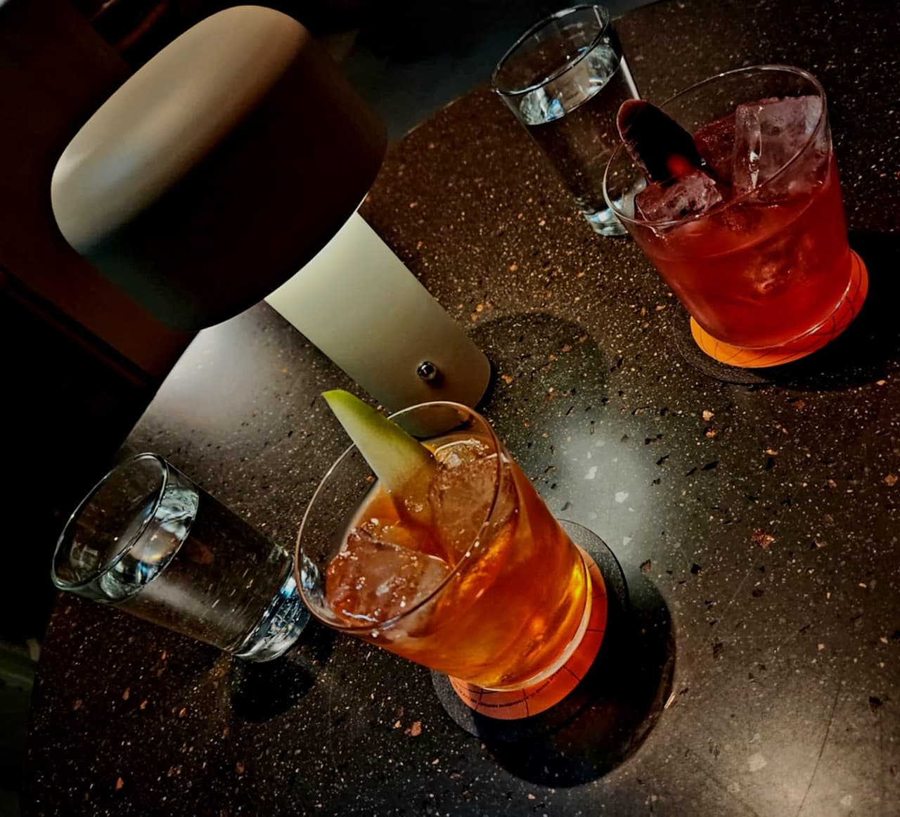 Two cocktails on a dimly lit table with a modern lamp. in London
