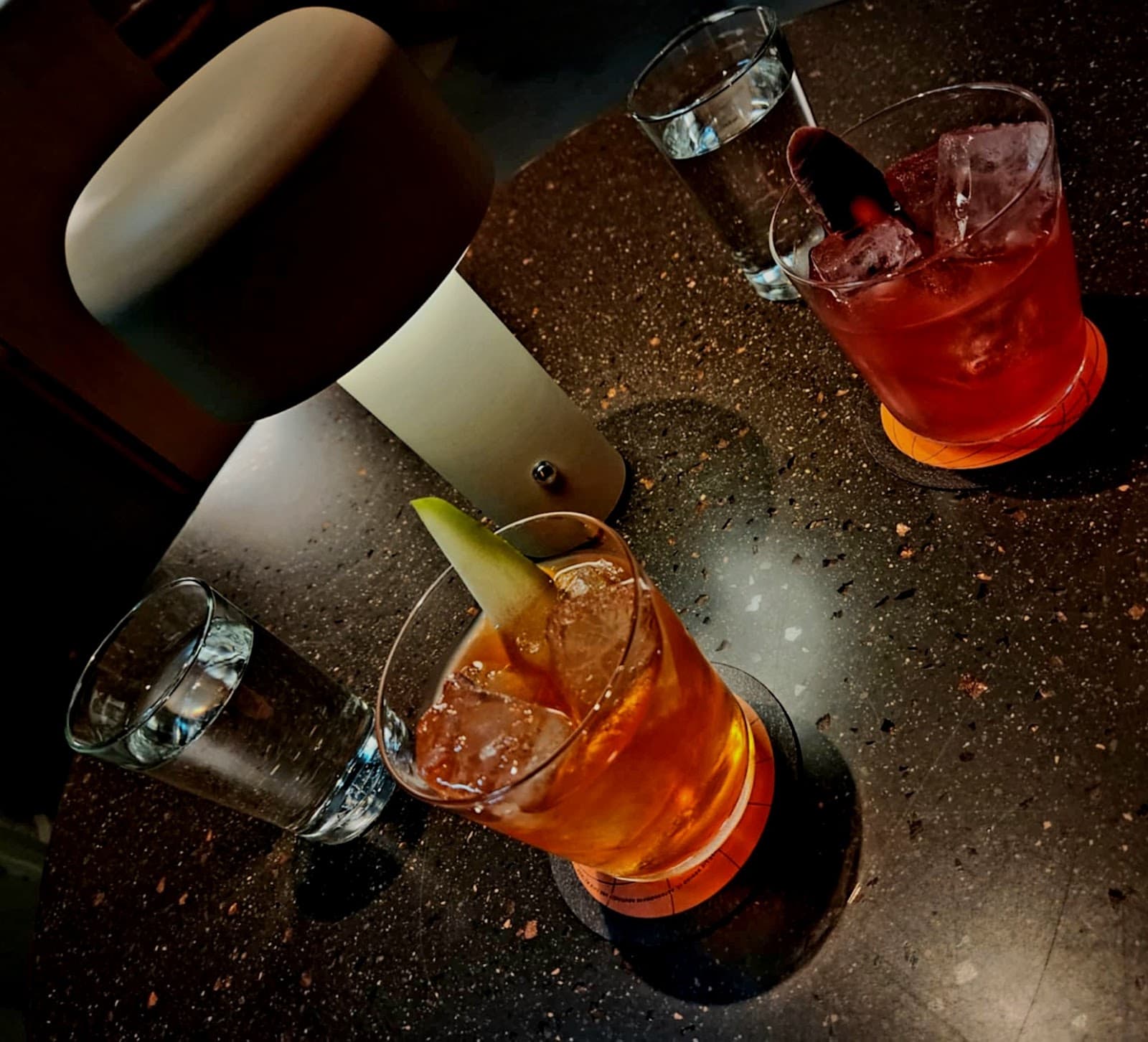 Two cocktails on a dimly lit table with a modern lamp. in London