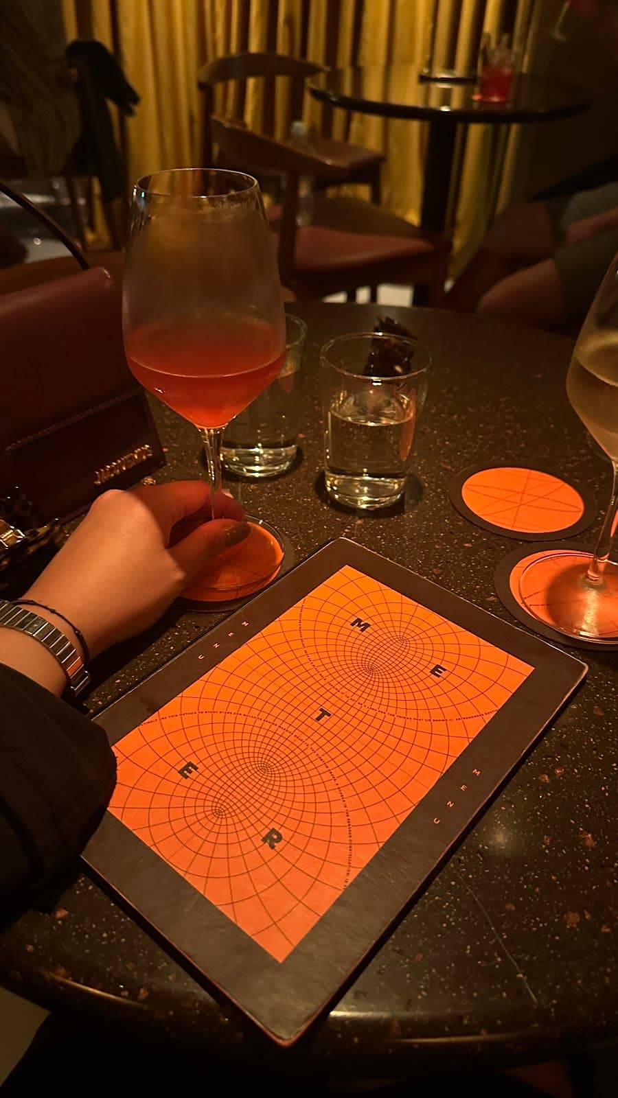 Person holding a cocktail glass at a bar table with menu and drinks in London