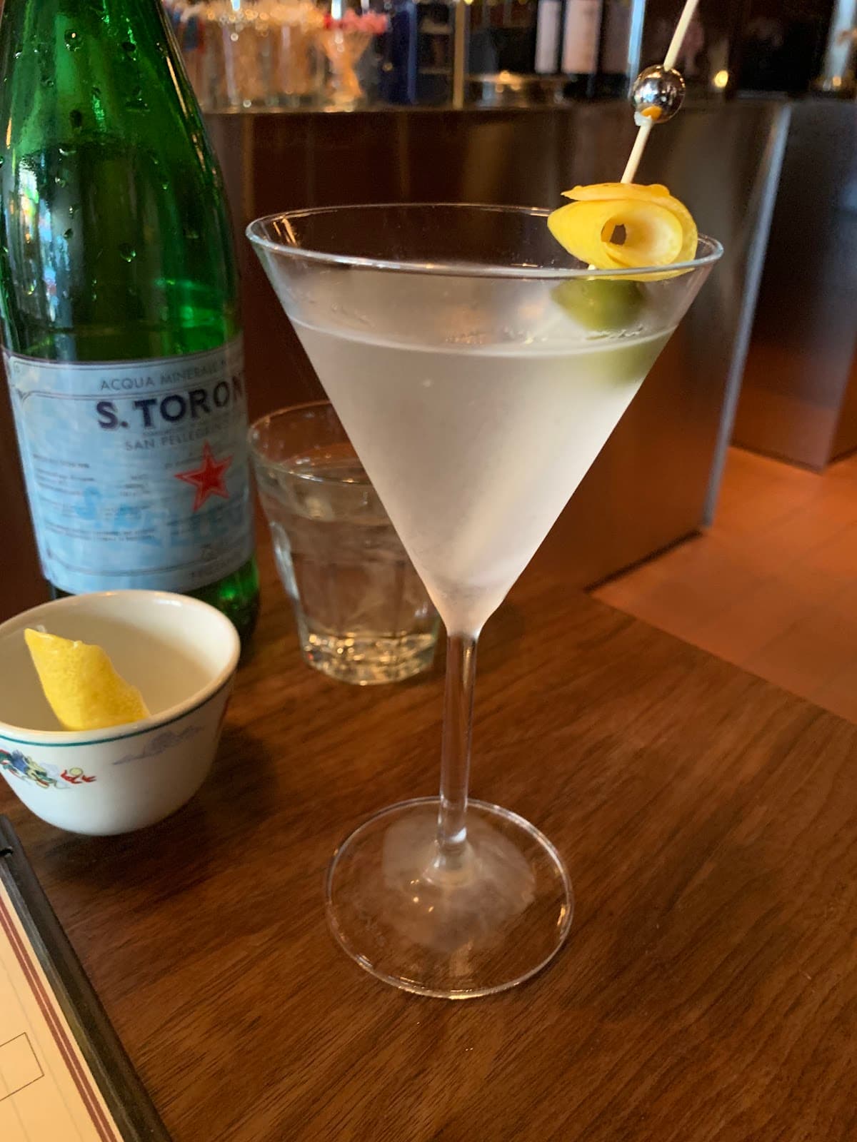 Martini glass with lemon twist and olive on wooden table at bar in Toronto