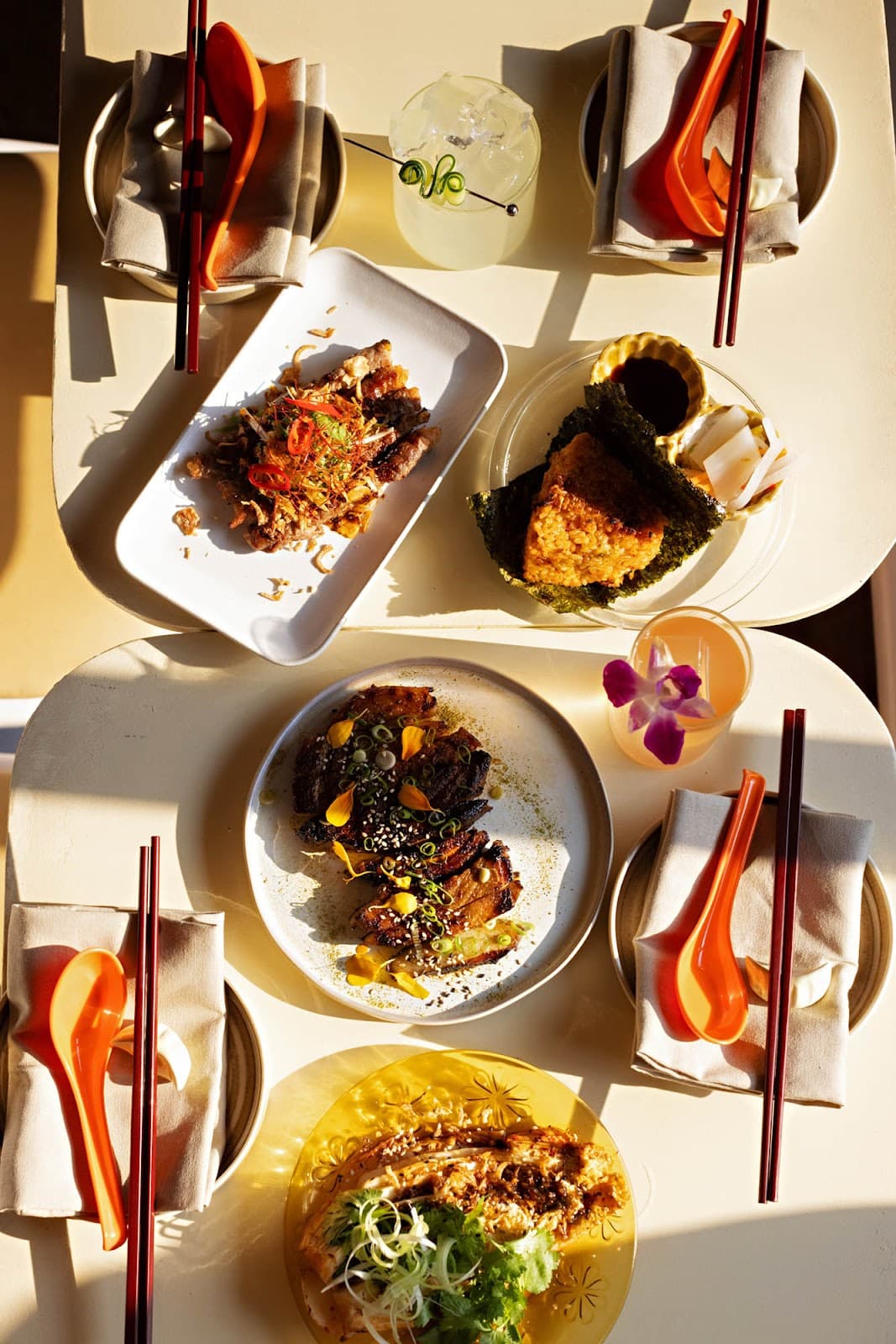 Top-down view of assorted dishes with two cocktails on a sunlit table in Toronto