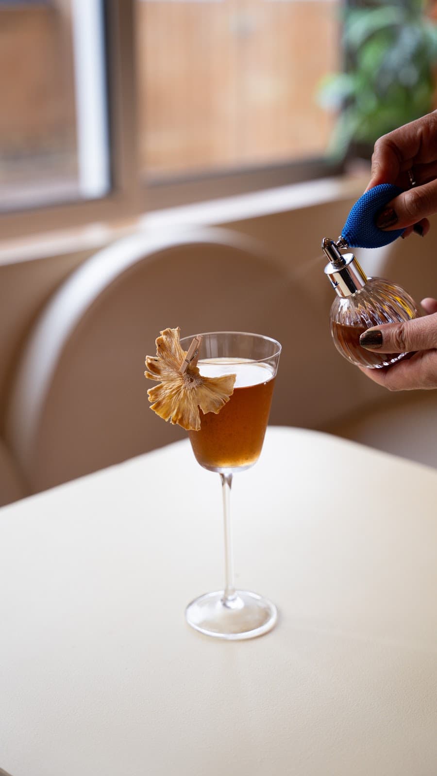 Close-up of a cocktail with a dried pineapple garnish and a hand using a spray bottle in Toronto