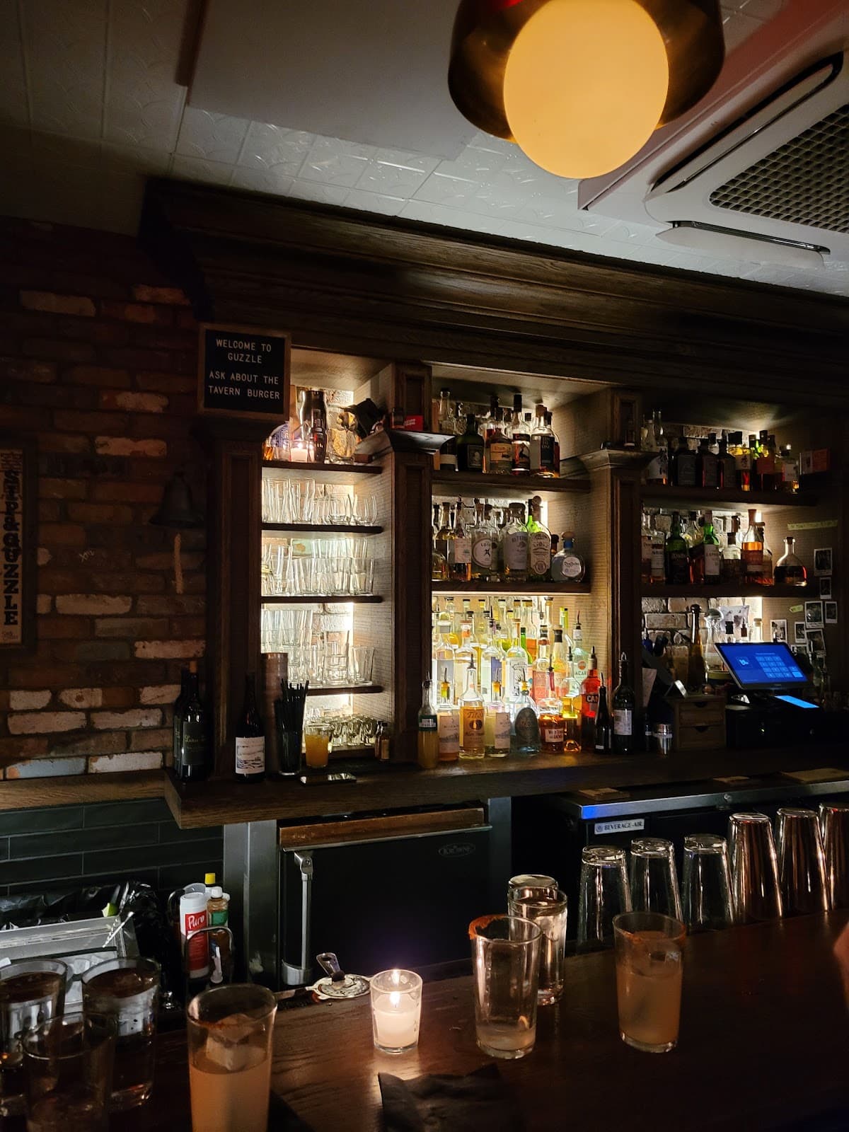 Dimly lit bar with bottles and glasses on shelves and a wooden counter in New York