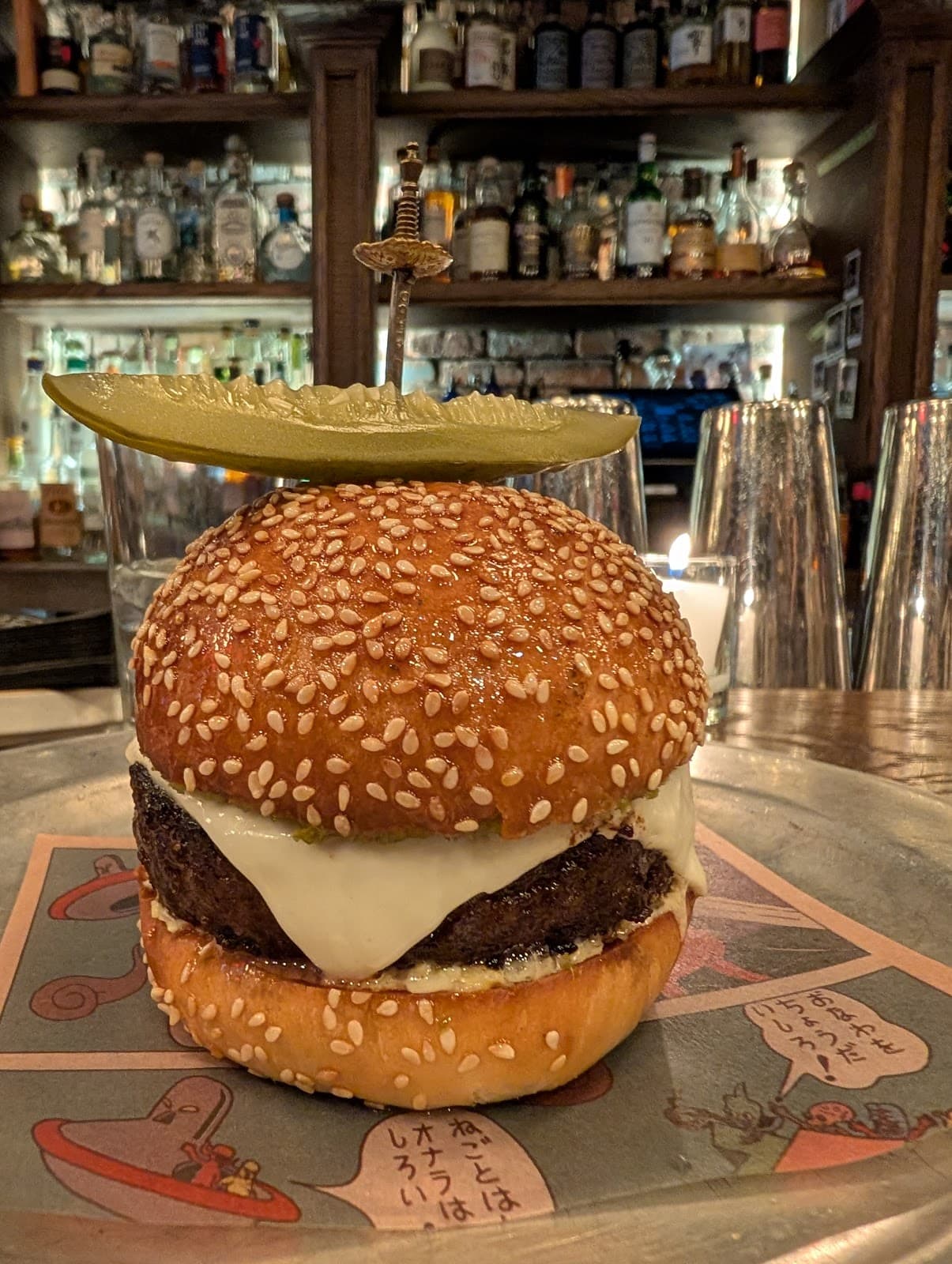 Burger in front of a well-stocked bar with pickle garnish on top in New York