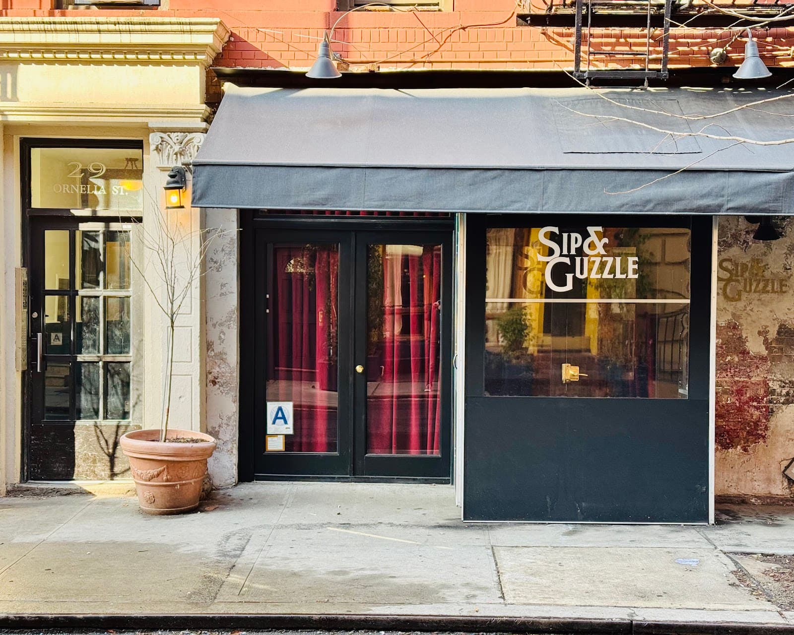 Exterior of Sip & Guzzle with a black awning and red curtains