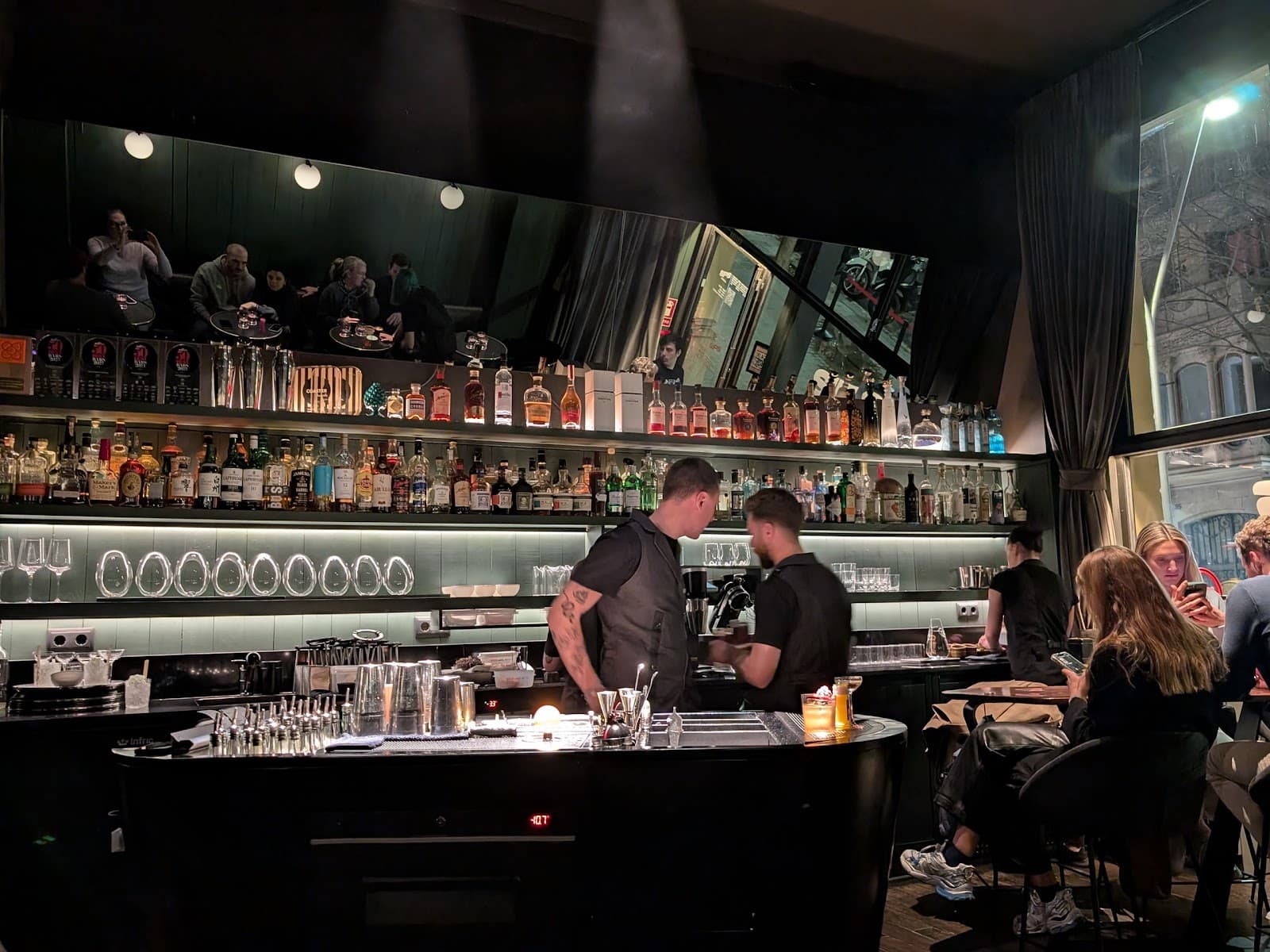 Well-stocked bar with patrons and bartenders in a dimly lit upscale setting in Barcelona