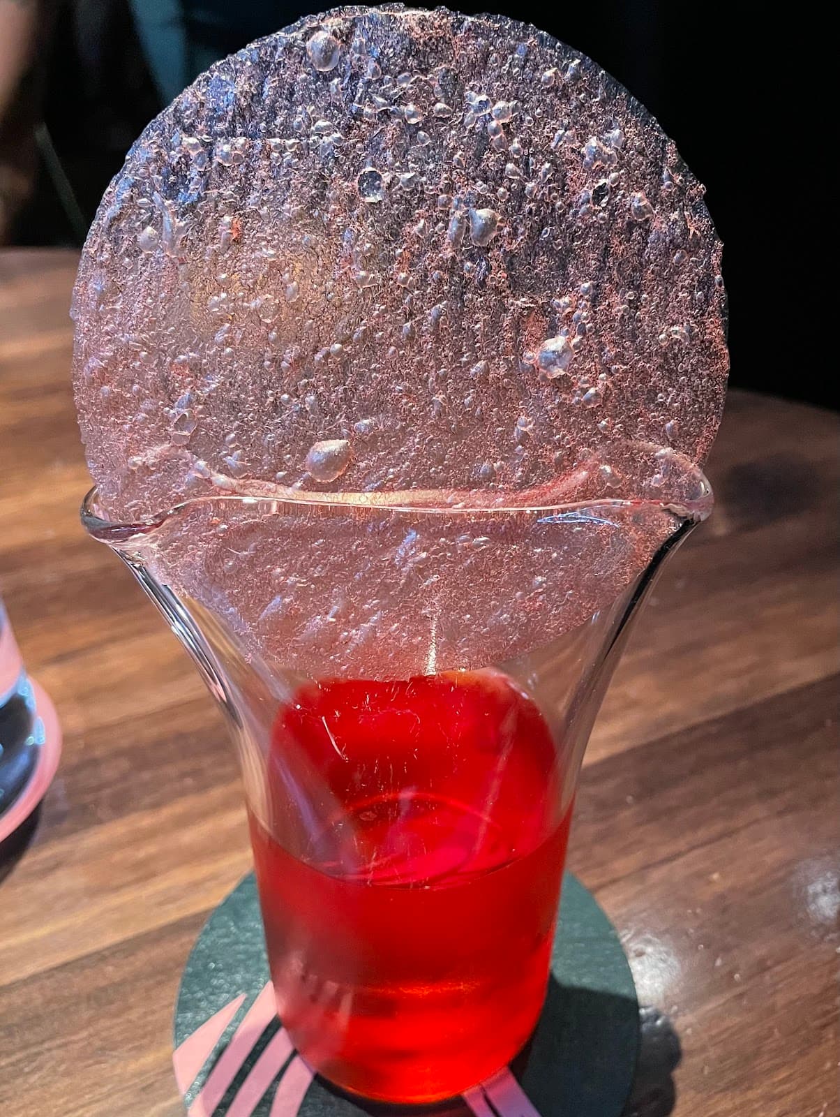 Red cocktail with a textured ice disc on top in a glass in Barcelona