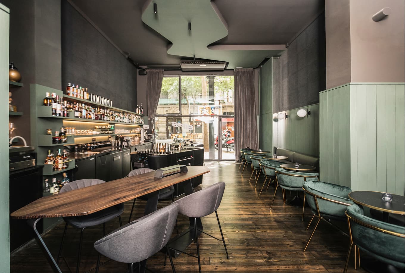 Modern cocktail bar interior with green accents and large windows