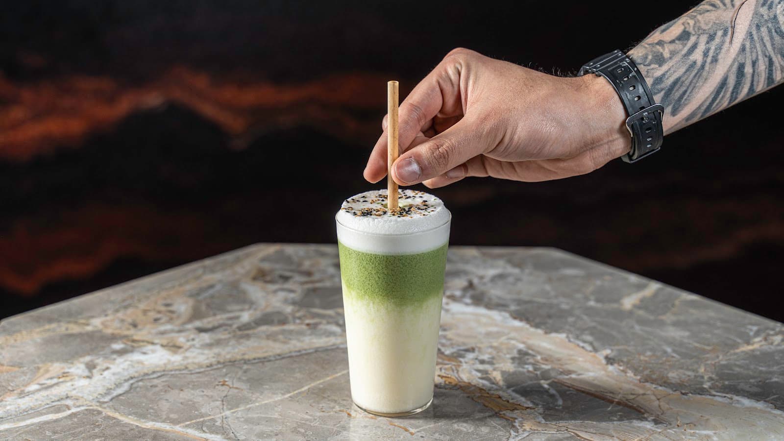 Tattooed hand placing straw in creamy green and white cocktail on marble table in Toronto