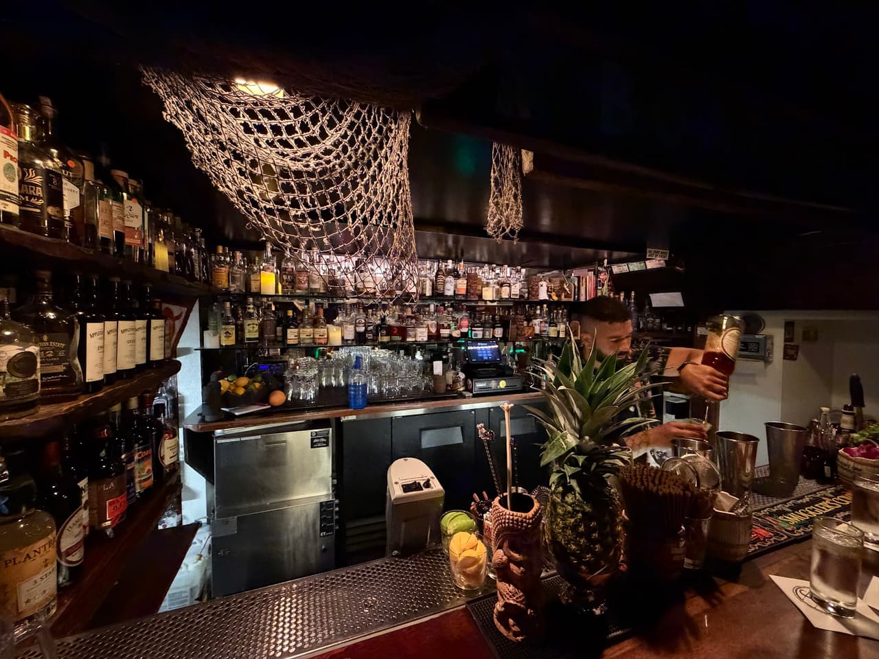 Bartender mixing drinks at a dimly lit, cozy bar with pineapple decor in San Francisco