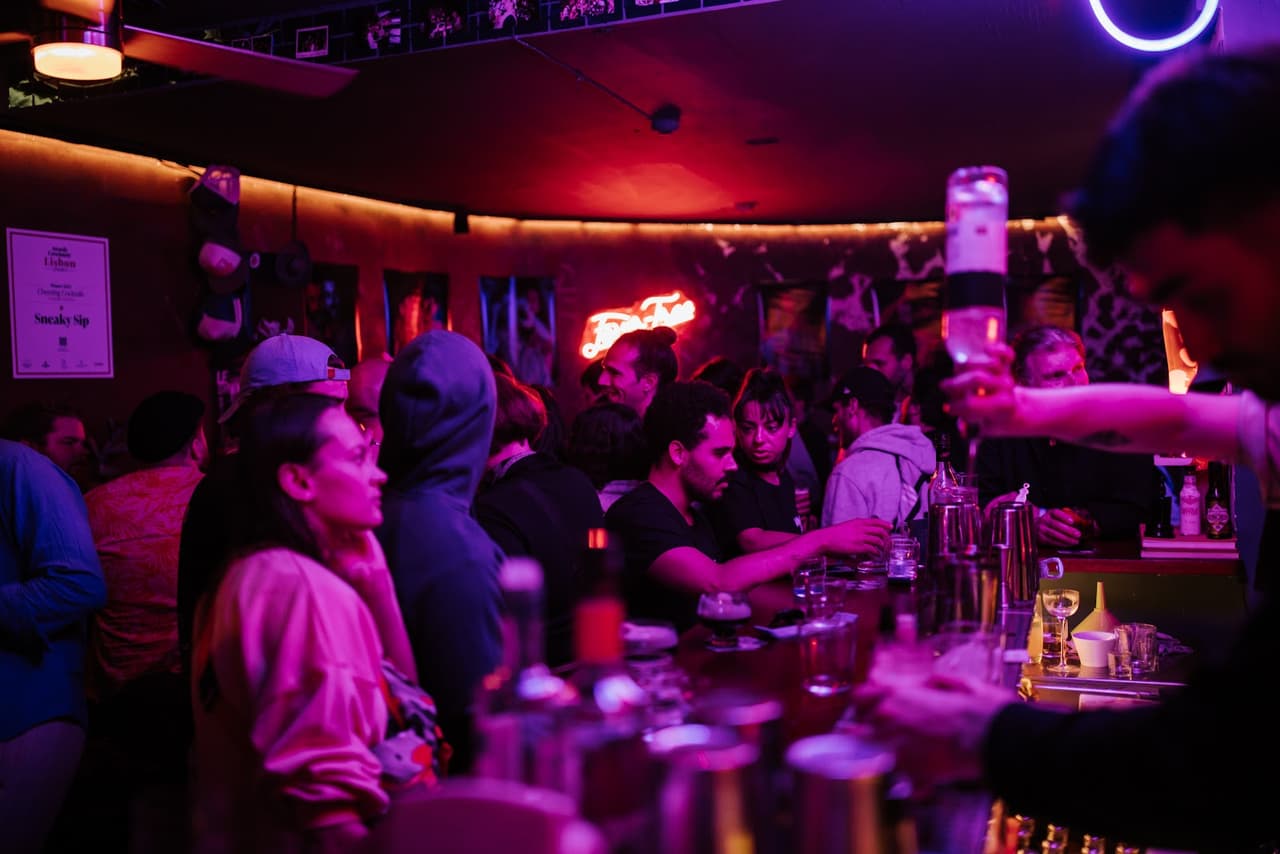 Dimly lit bar with patrons and neon lights creating a lively atmosphere in Lisboa