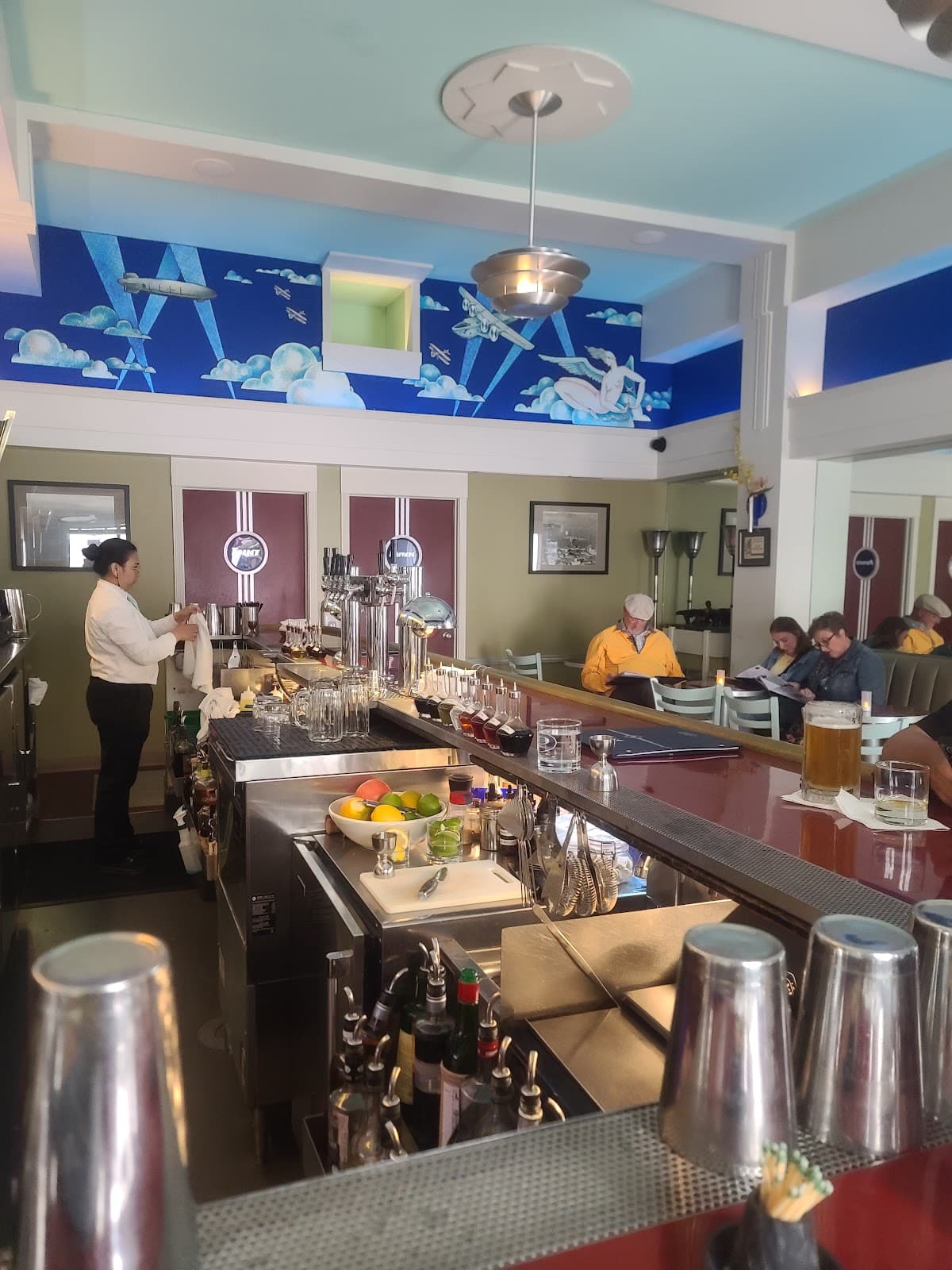 Art deco style bar with colorful ceiling mural and bartender serving drinks in San Francisco