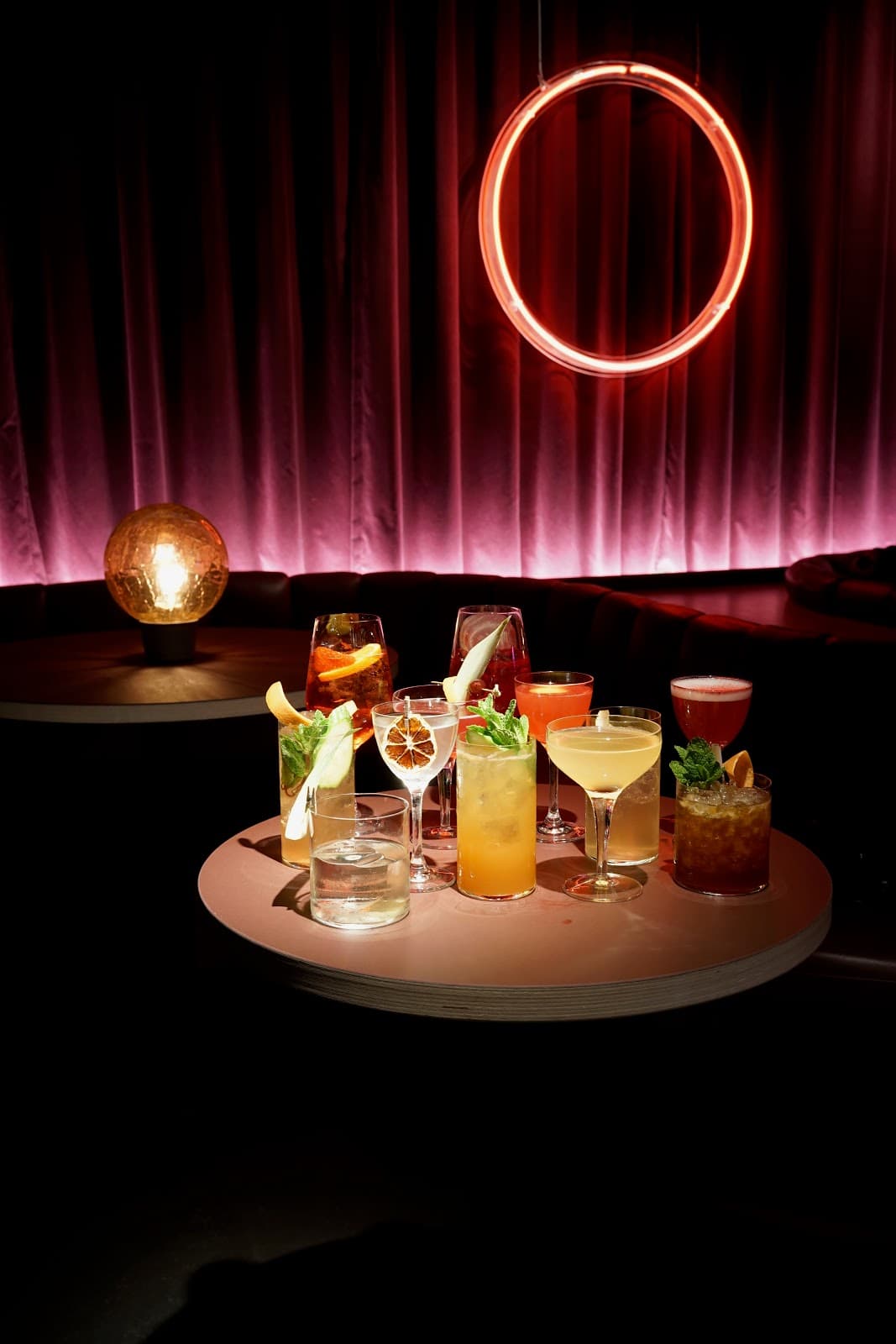 Assorted cocktails on a table with a neon circle and dim lighting in London