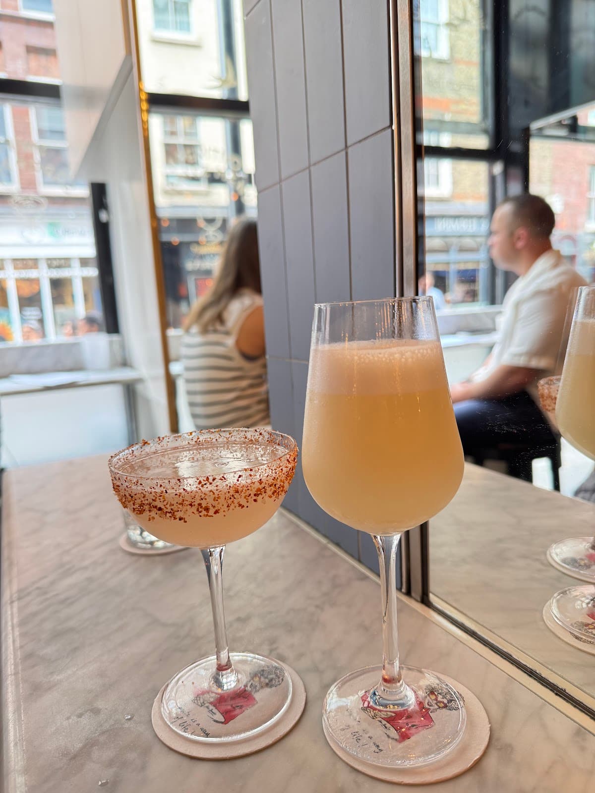 Two cocktails on a marble table in front of a window at a bar in London