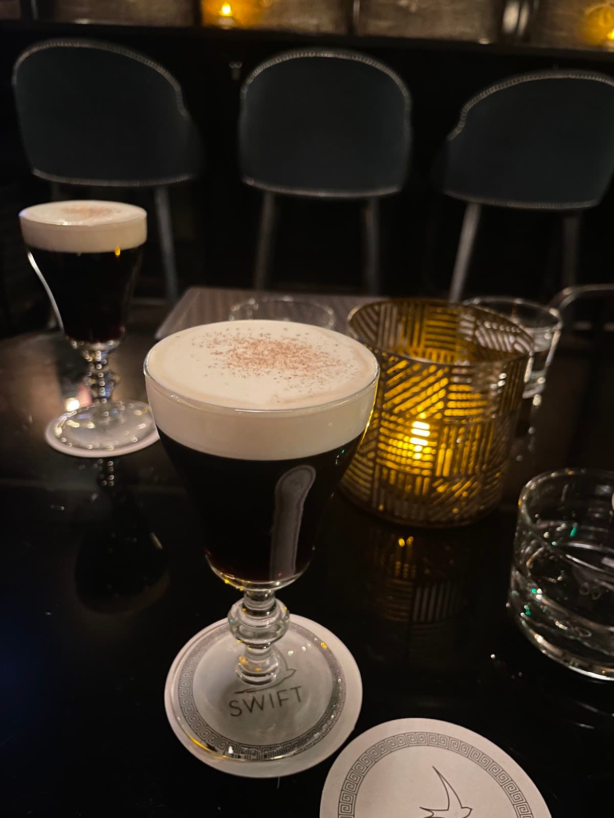 Cocktail glasses with dark drinks and creamy tops on bar table at Swift in London