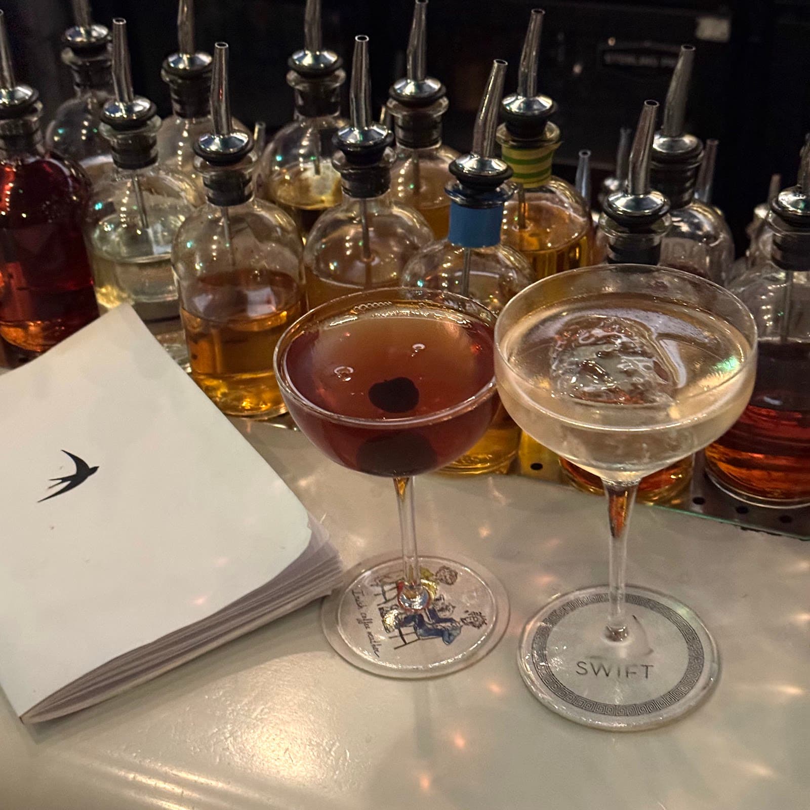 Two cocktails on a bar with bottles in the background at Swift in London