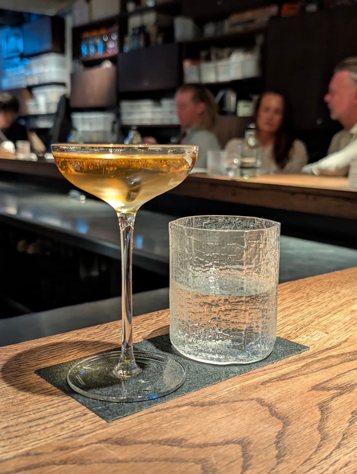 Close-up of a cocktail glass and water tumbler on a wooden bar counter in London