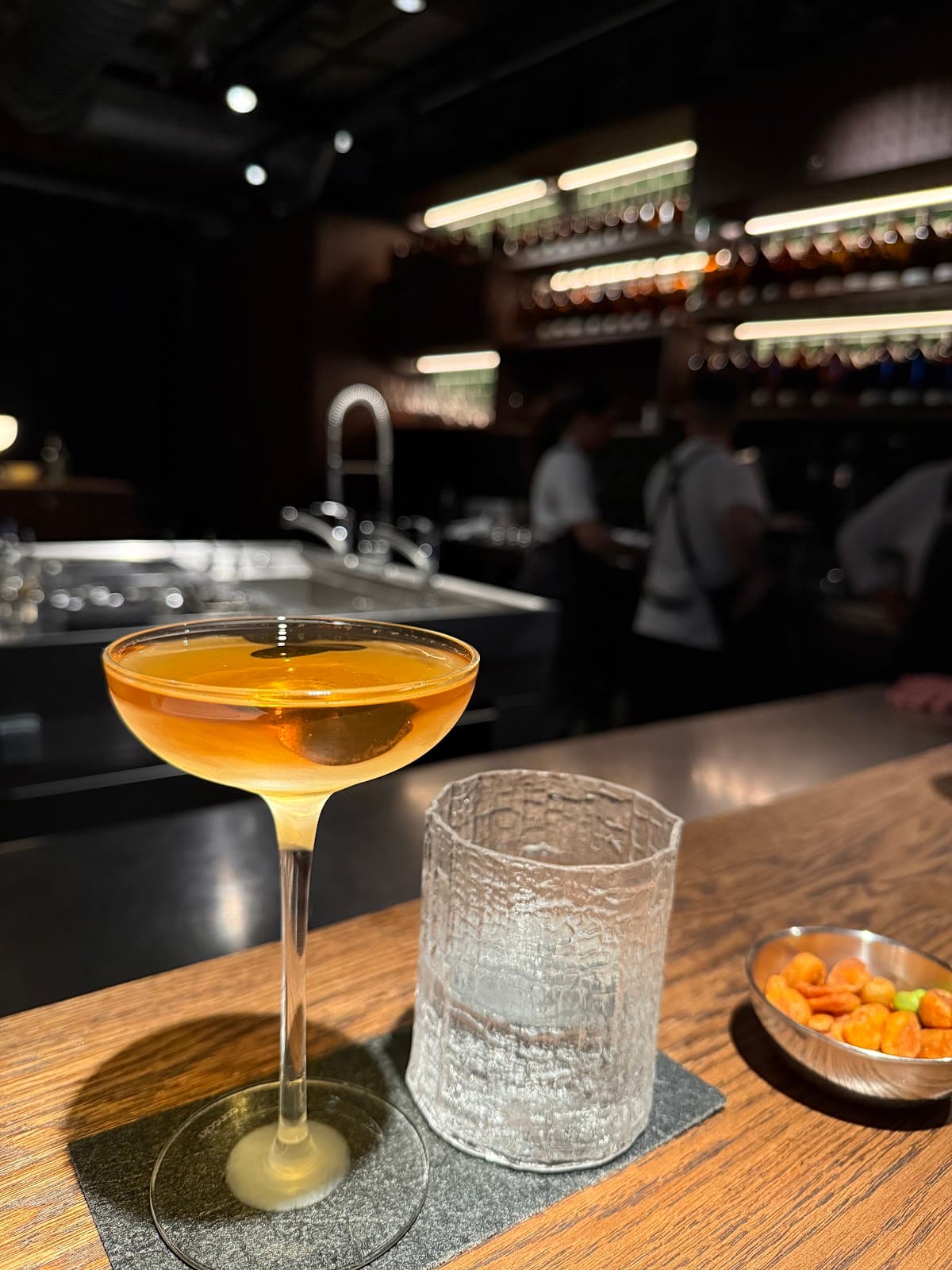 Close-up of cocktail on wooden bar with snacks and glass in upscale setting. in London