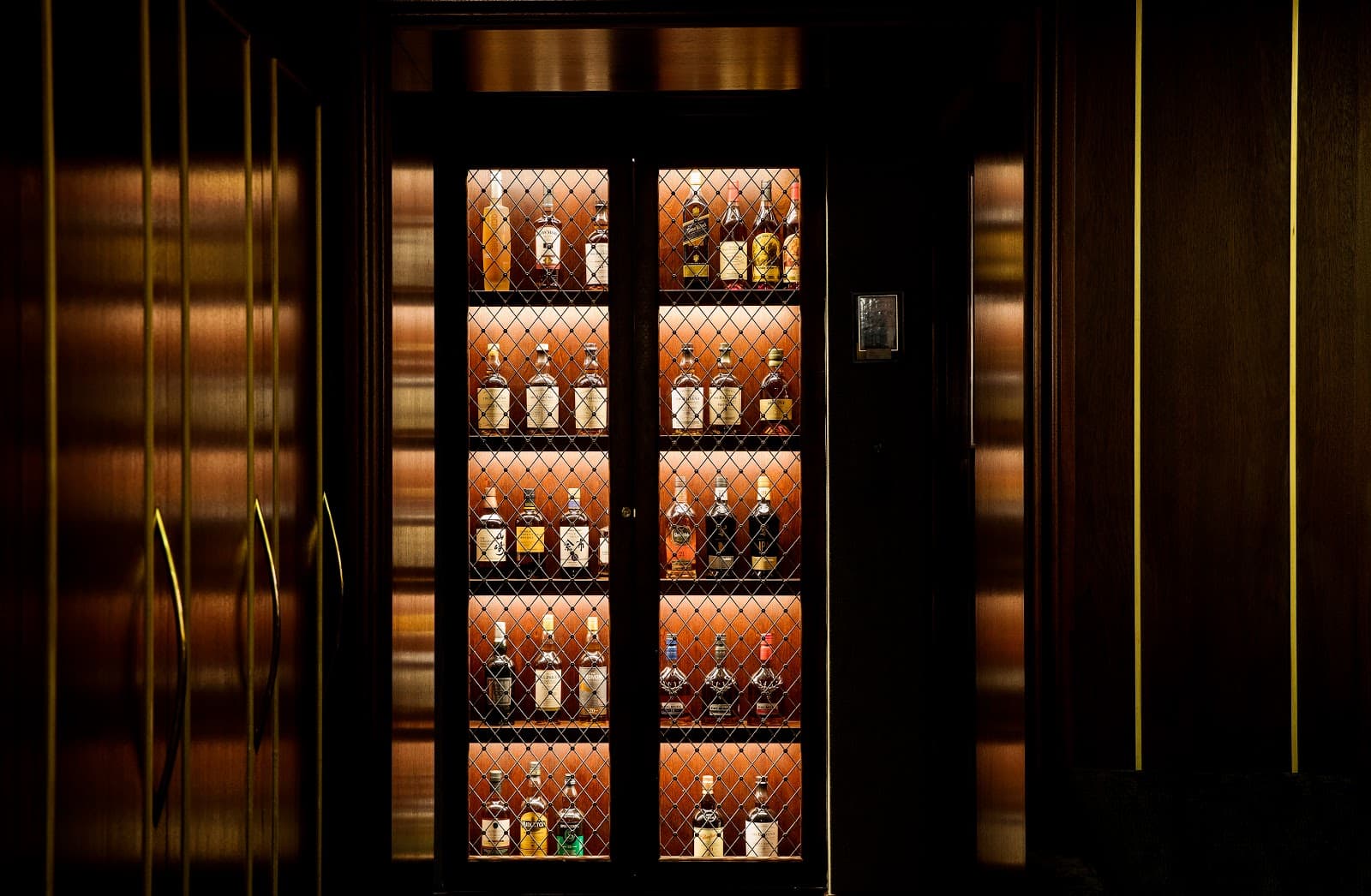 Elegant display of liquor bottles in a dimly lit wooden cabinet in London