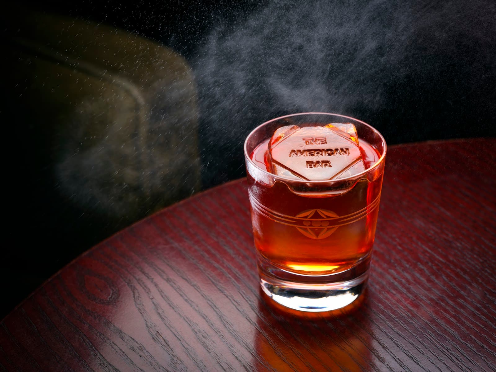 Close-up of a cocktail on a dark wooden table with engraved ice cube in London