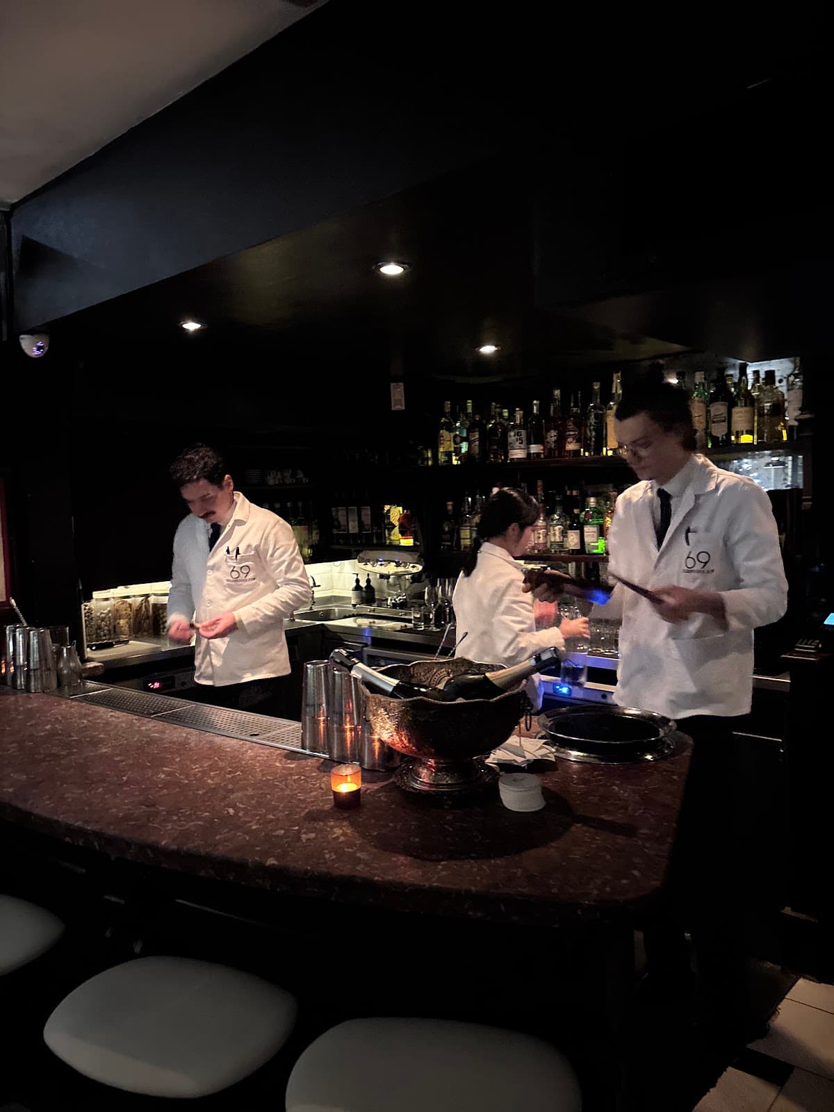 Bartenders working behind a dimly lit bar with bottles on shelves in London