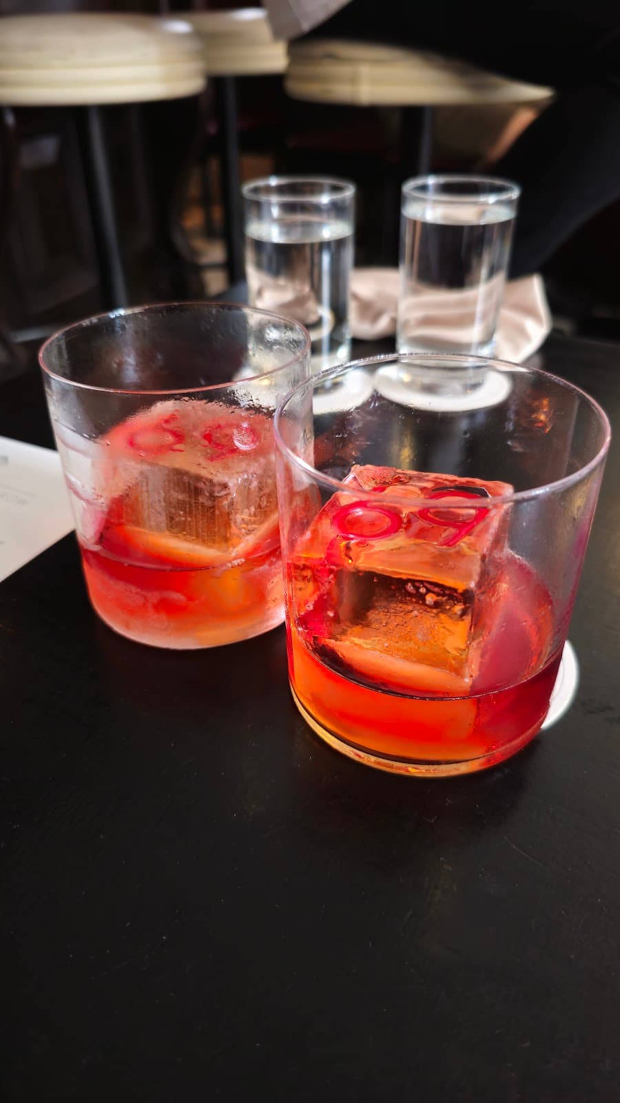 Two cocktails with large ice cubes on a dark table at a bar in London