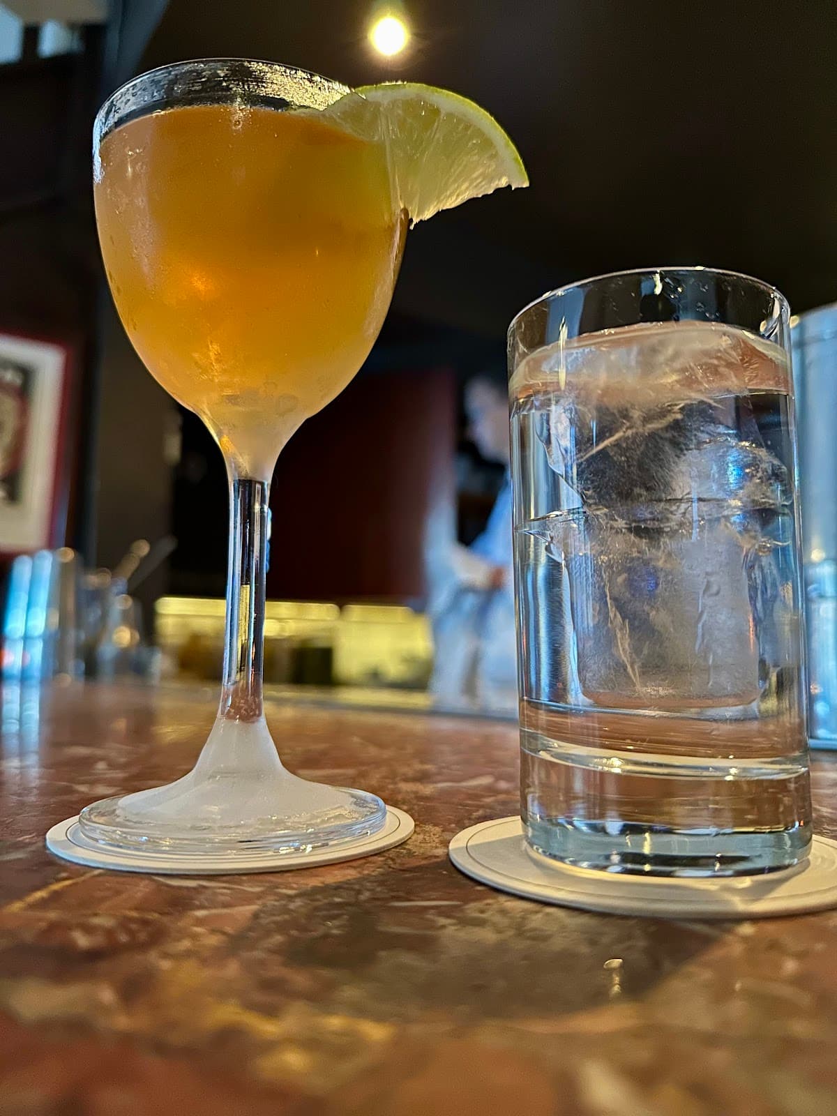 Close-up of a cocktail with a lime wedge and a glass of water on a bar counter in London